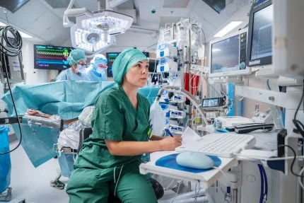 Medical professionals wearing scrubs and masks working in a hospital operating room with monitors and medical equipment.