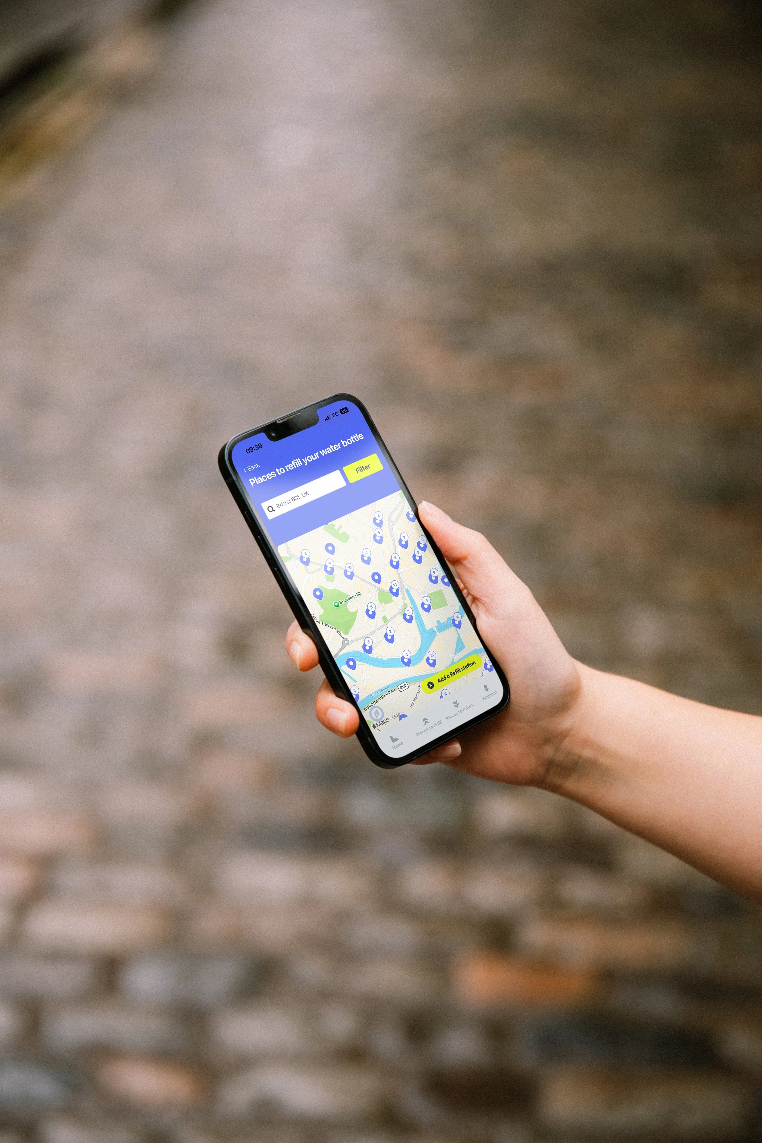 A person holding a smartphone with a map and water bottle refill station app on the screen, outdoors on a stone pathway.