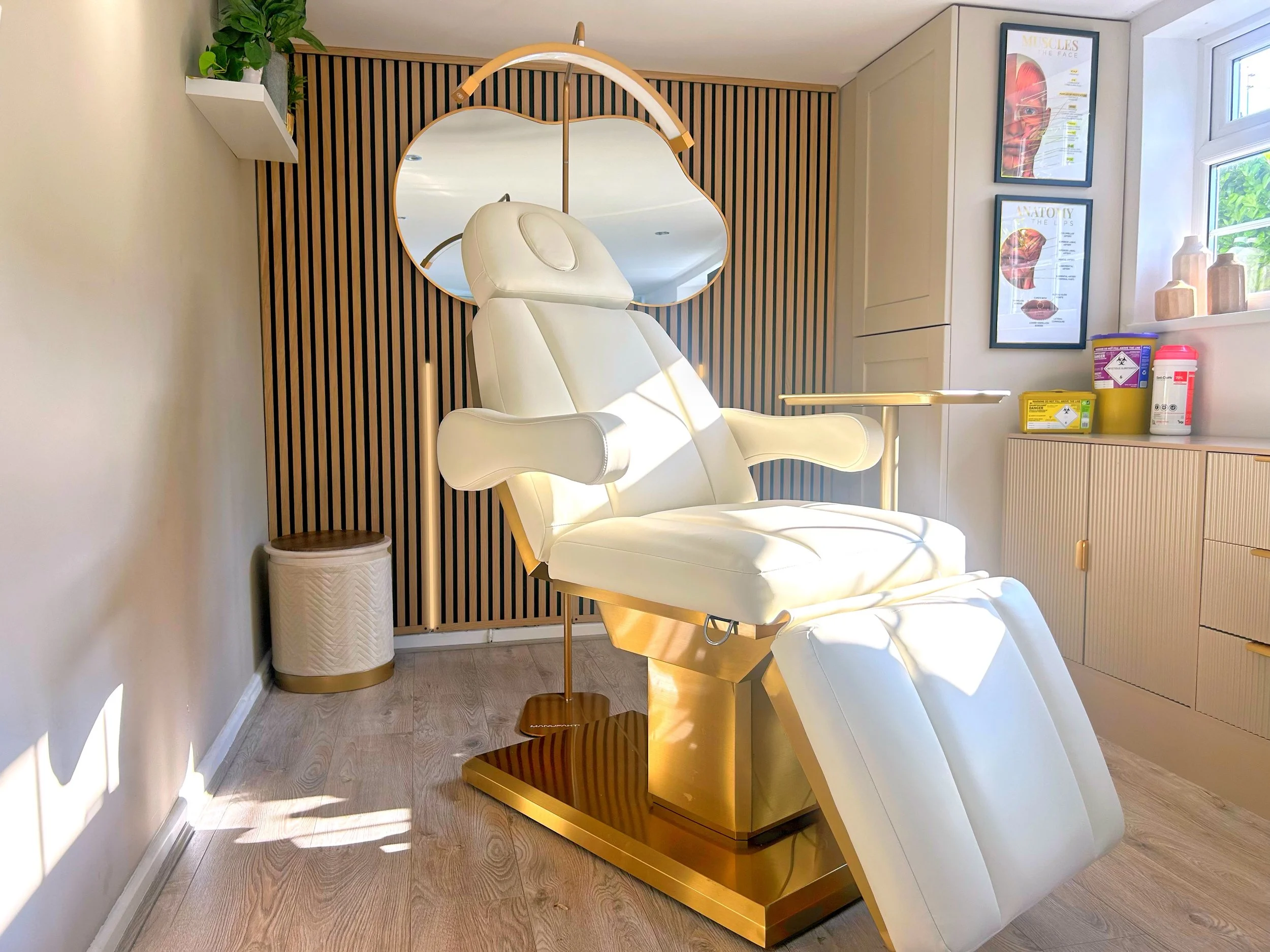 Treatment room at North Glow Aesthetics with the gold treatment chair, mirror, anatomy posters, and clinical waste storage, Norden, Rochdale.