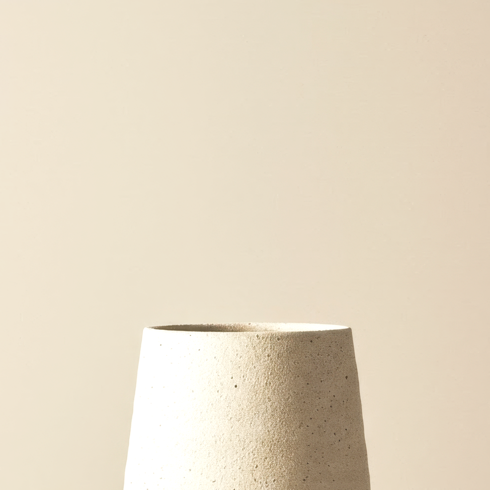Close-up of a textured, white ceramic vase against a plain, neutral background.