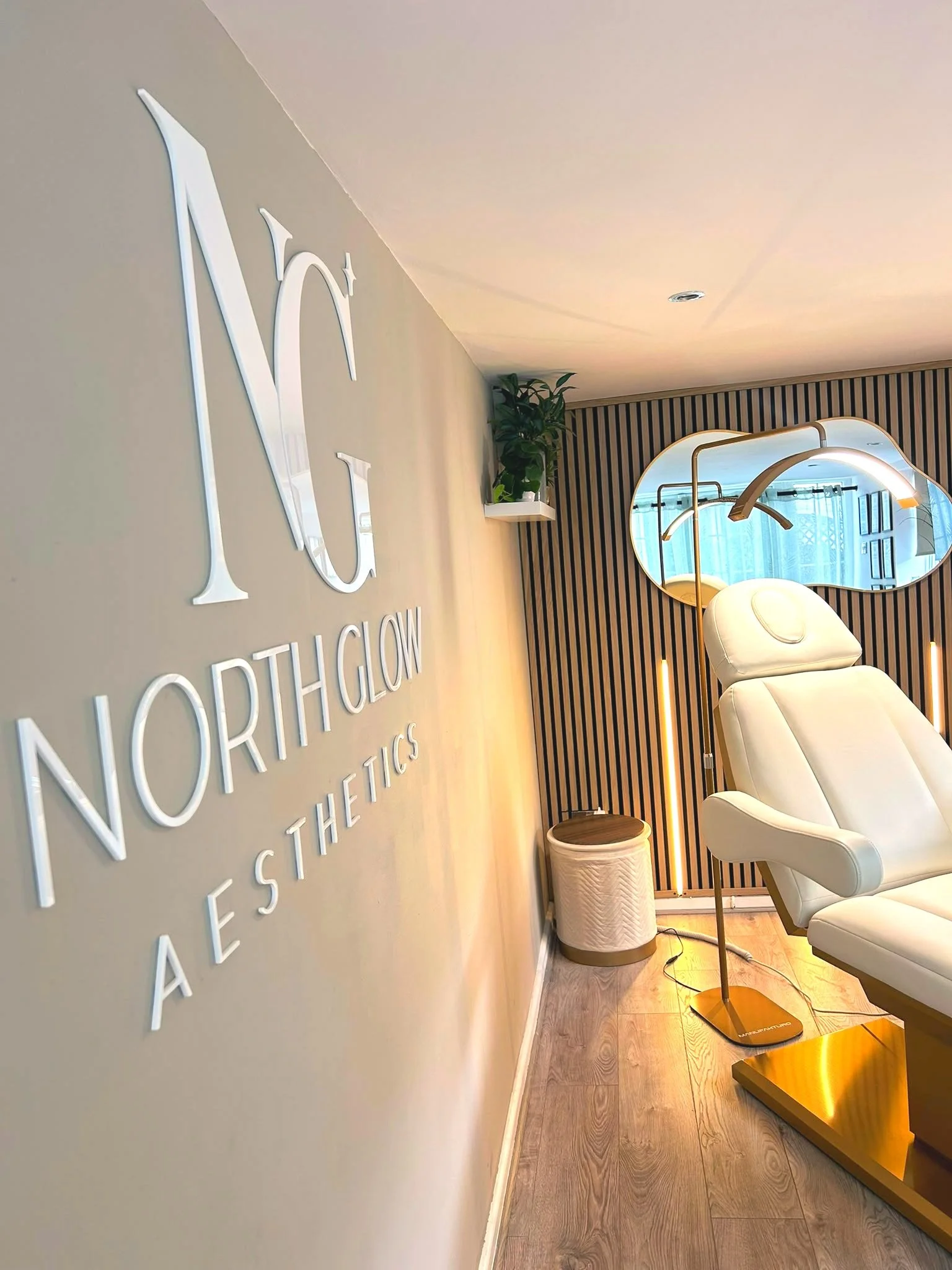 North Glow Aesthetics wall logo viewed from the corridor, with the treatment chair and mirror visible beyond, Norden, Rochdale.