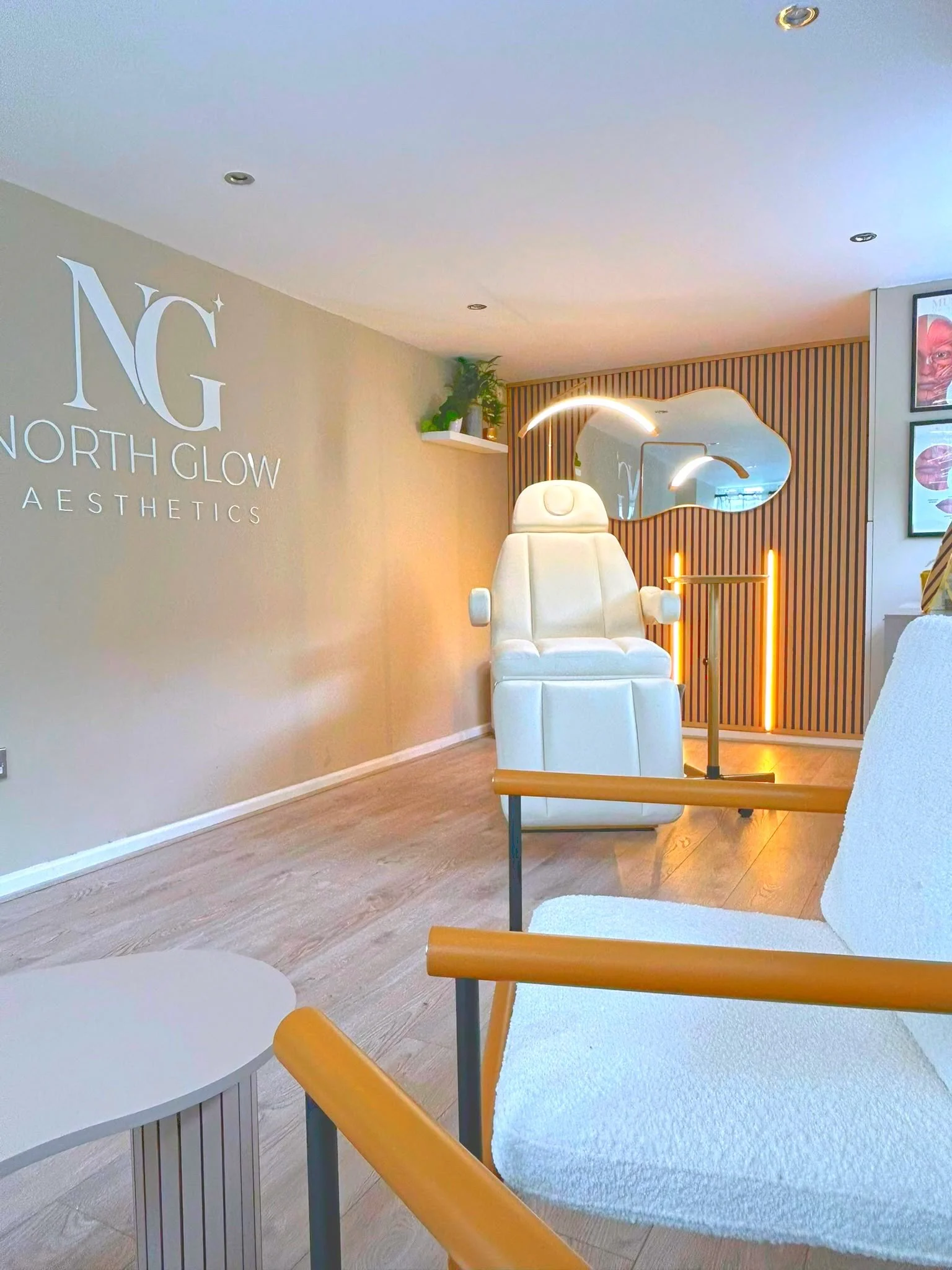 Reception area at North Glow Aesthetics showing the branded display screen, boucle armchairs, and accreditation certificates, Norden, Rochdale.