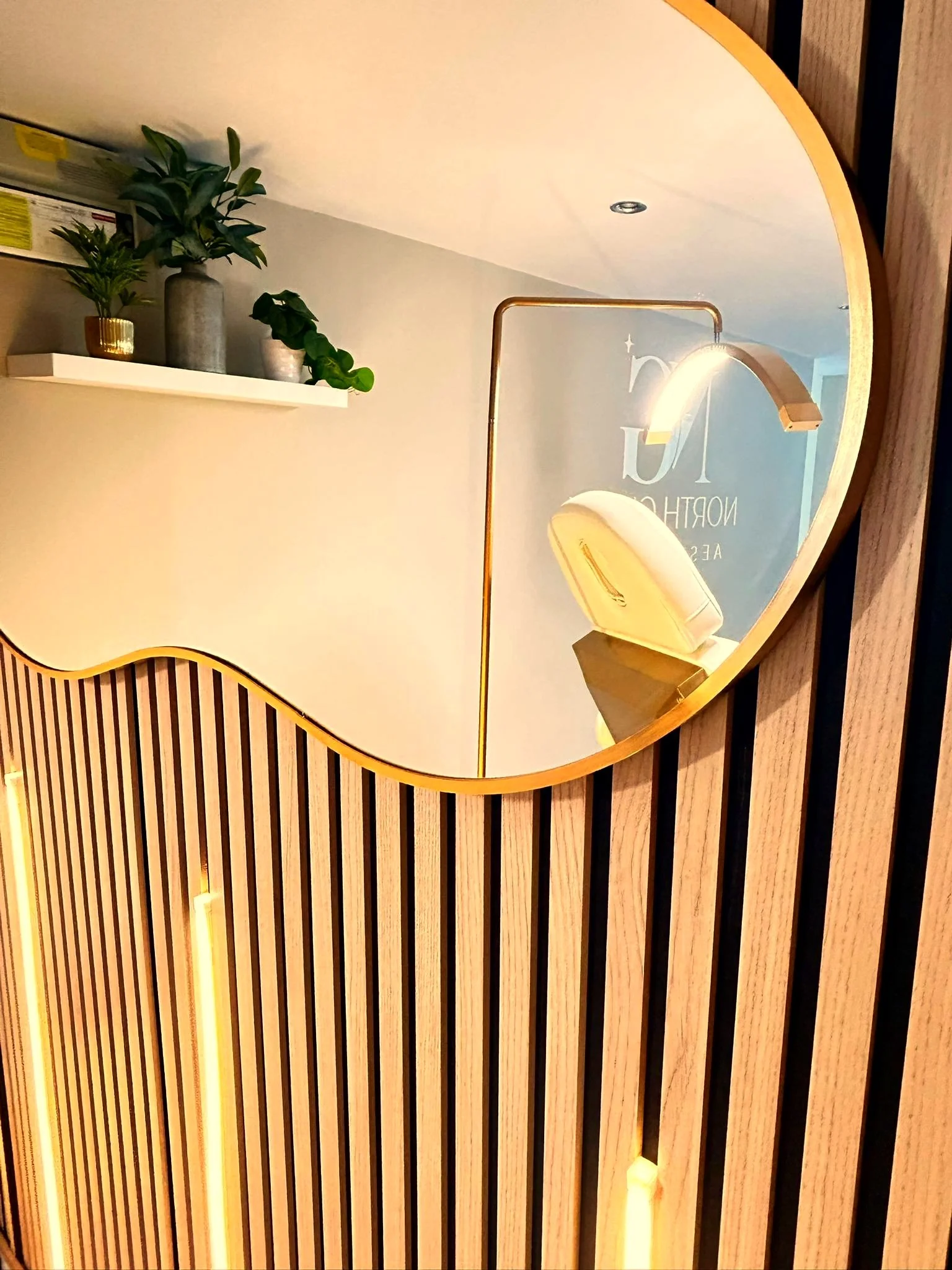 Organic cloud-shaped mirror on the slatted wood wall at North Glow Aesthetics, reflecting the adjoining lounge area, Norden, Rochdale.