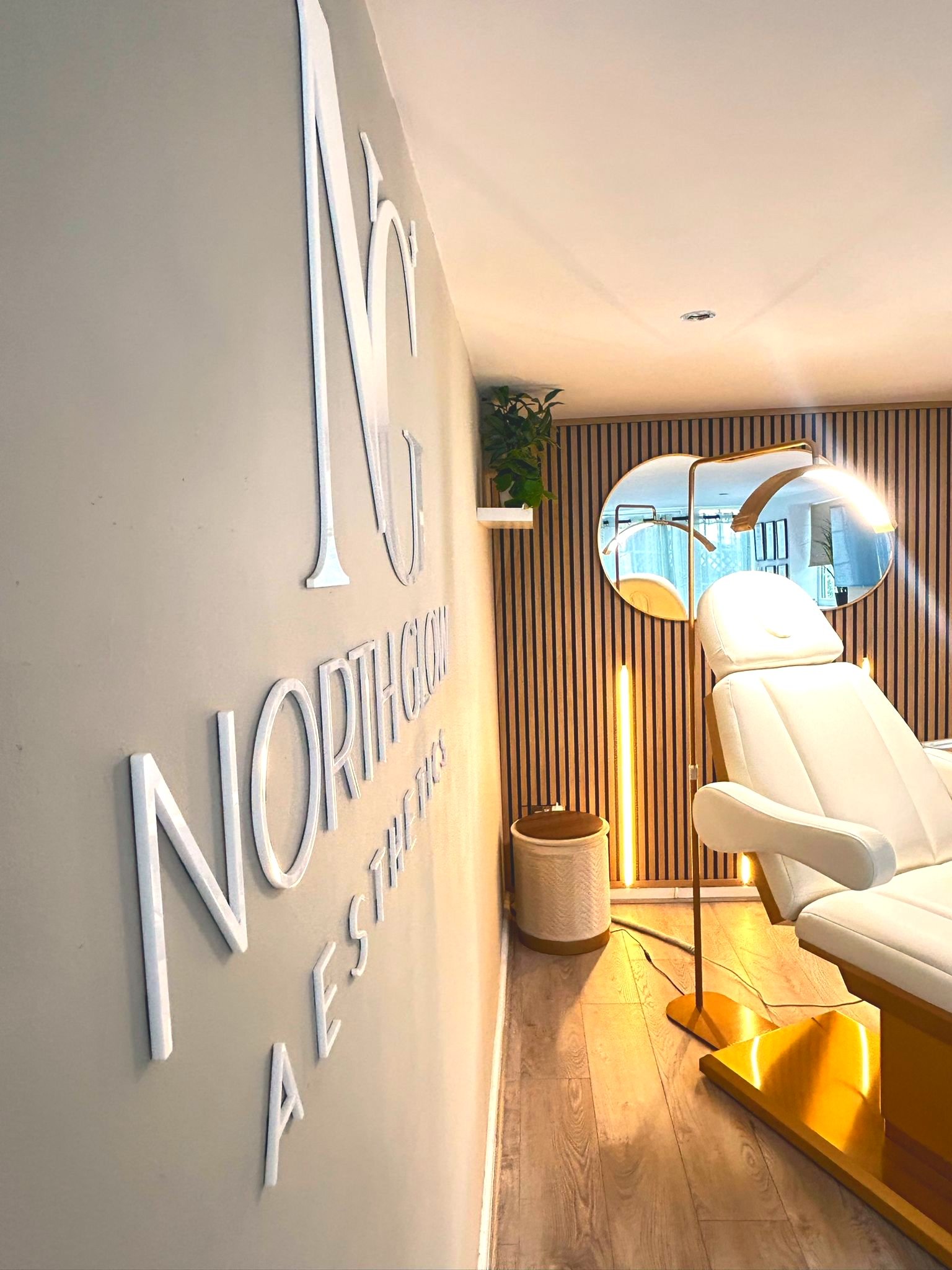 3D NG North Glow Aesthetics wall lettering viewed down the corridor, with the treatment chair and arc lamp beyond, Norden, Rochdale.