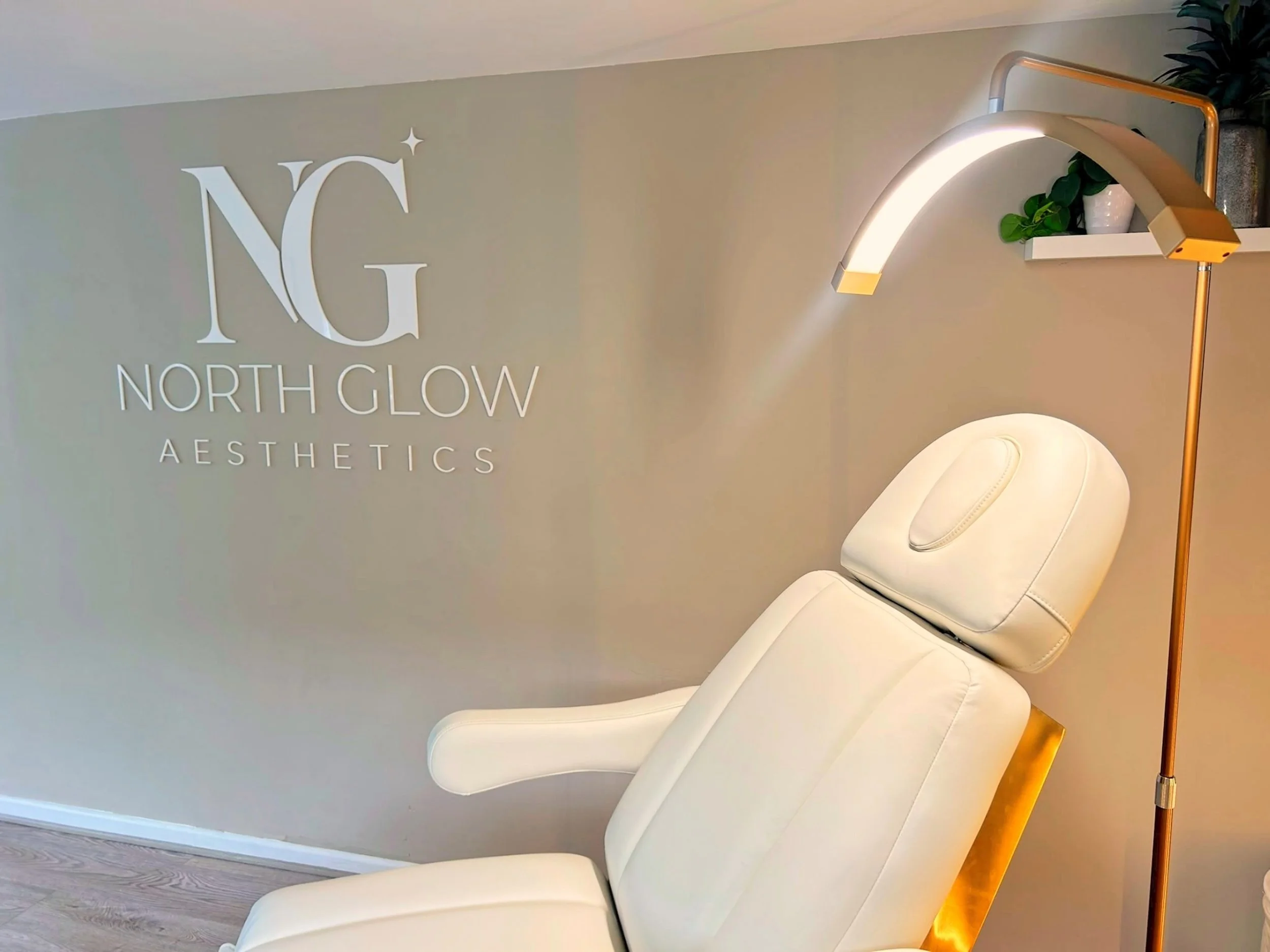 North Glow Aesthetics wall logo beside the treatment chair headrest and gold arc lamp, Norden, Rochdale.