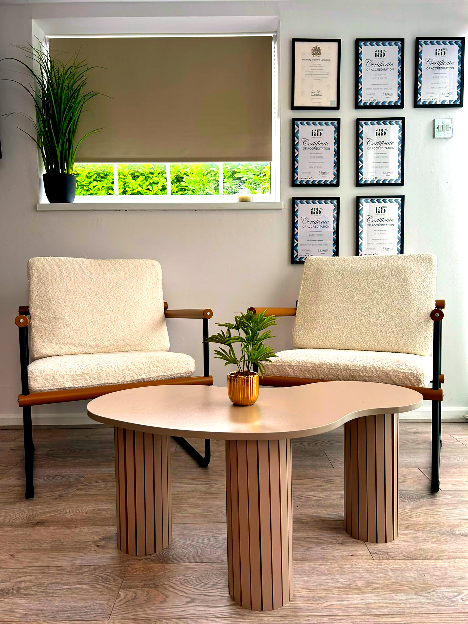 Consultation area at North Glow Aesthetics with boucle armchairs, a coffee table, and accreditation certificates, natural light from the garden doors, Norden, Rochdale.