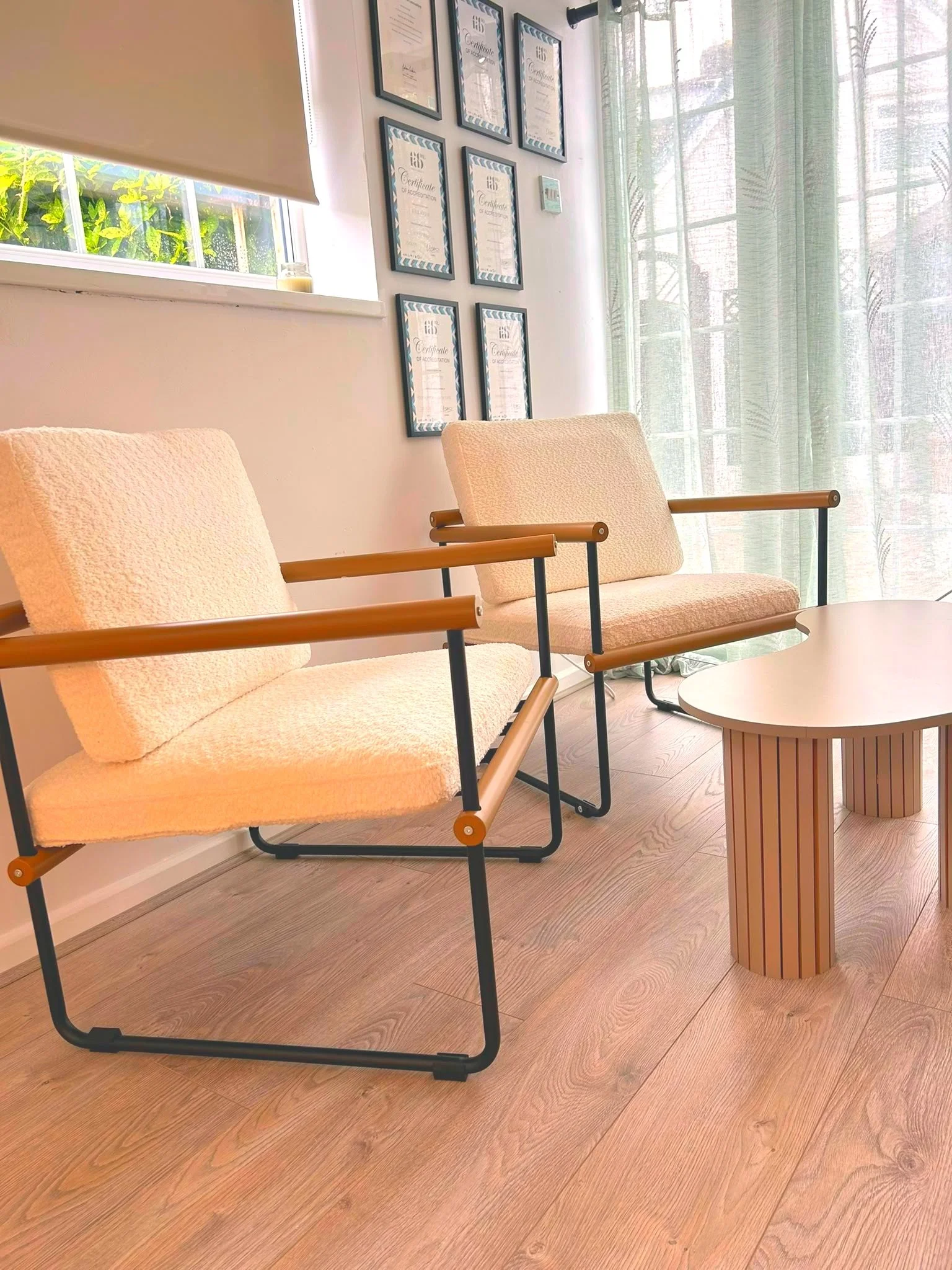 Side view of the consultation area at North Glow Aesthetics, with boucle armchairs, accreditation certificates, and natural light from the window, Norden, Rochdale.
