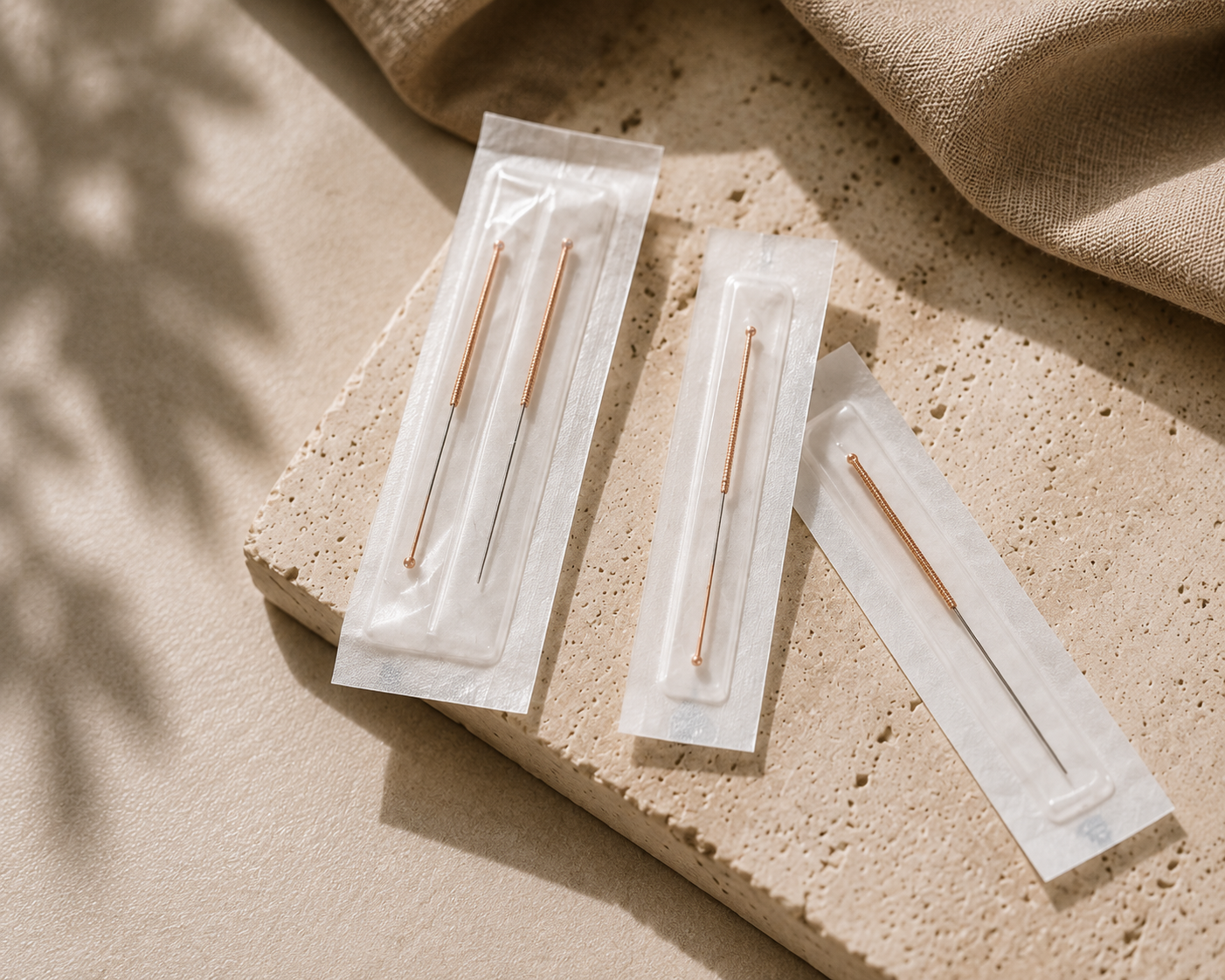 Drei Nähnadeln in Plastikhülsen auf einer beigen Steinunterlage, mit beige Stoff im Hintergrund.