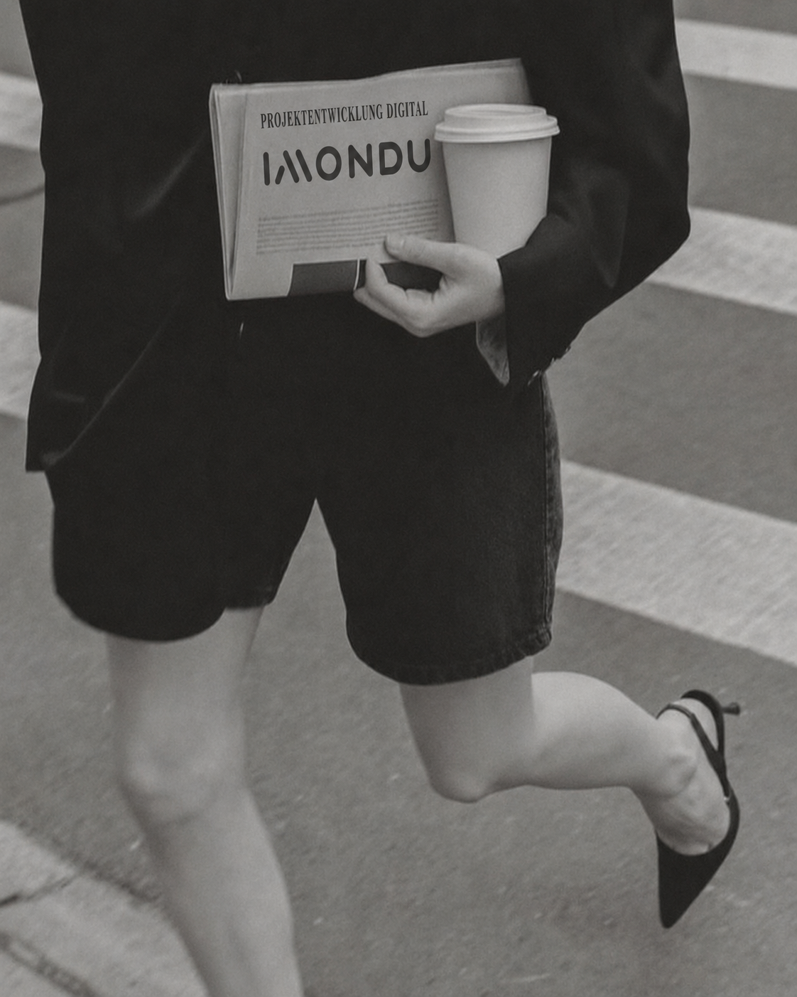 A person running on a crosswalk sidewalk, holding a coffee cup and a newspaper.