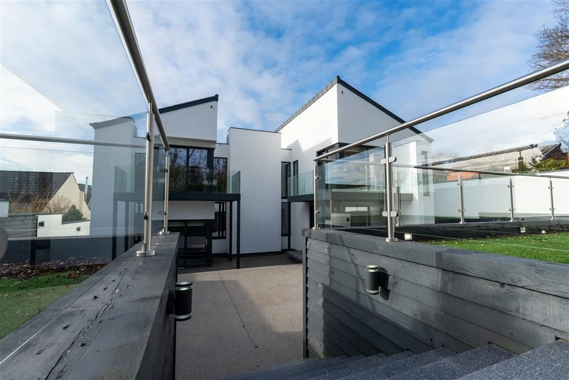 Modern white house with glass balcony railings, outside patio area, under a partly cloudy sky.