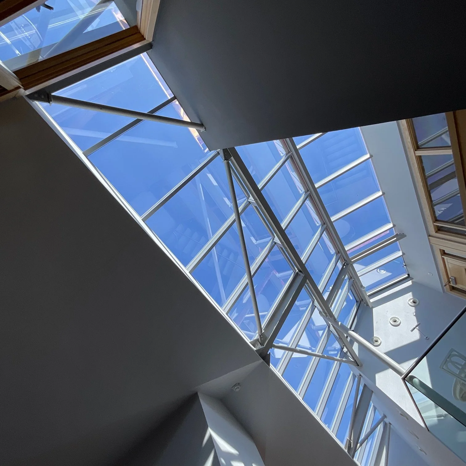 Interior view of a modern building with a glass ceiling and metal framework, sunlight streaming through.