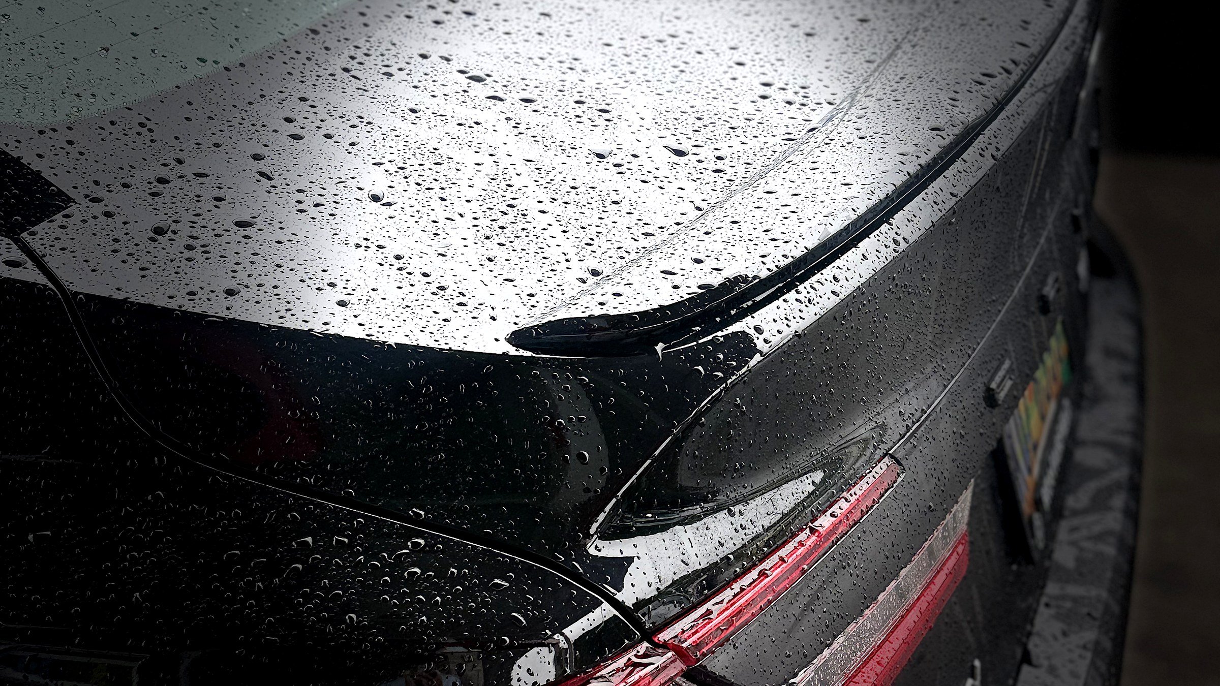 Close-up of the rear end of a black car with raindrops on the trunk and rear window.