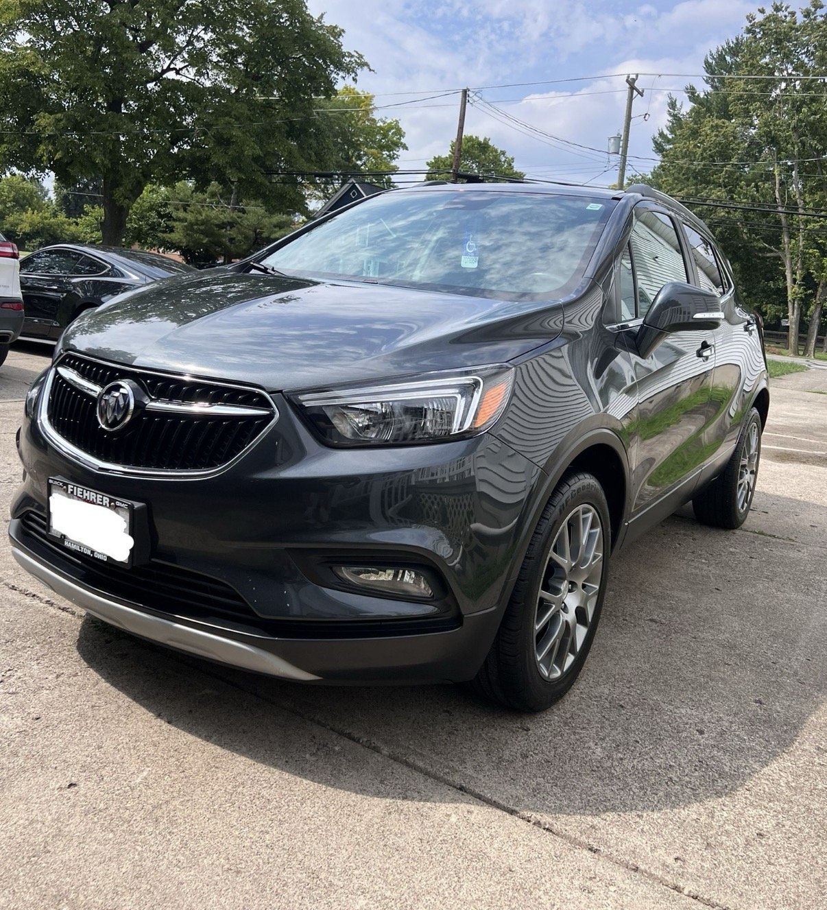 A black Buick SUV parked in a parking lot during daytime, with trees and other cars in the background.