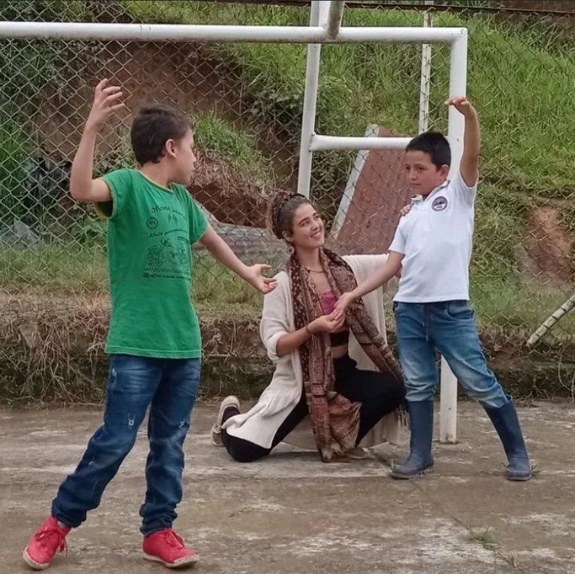 Two boys and a woman on a basketball court. The woman is kneeling between two boys, each with one arm raised. The boys are holding the woman's hands, and all three are smiling.