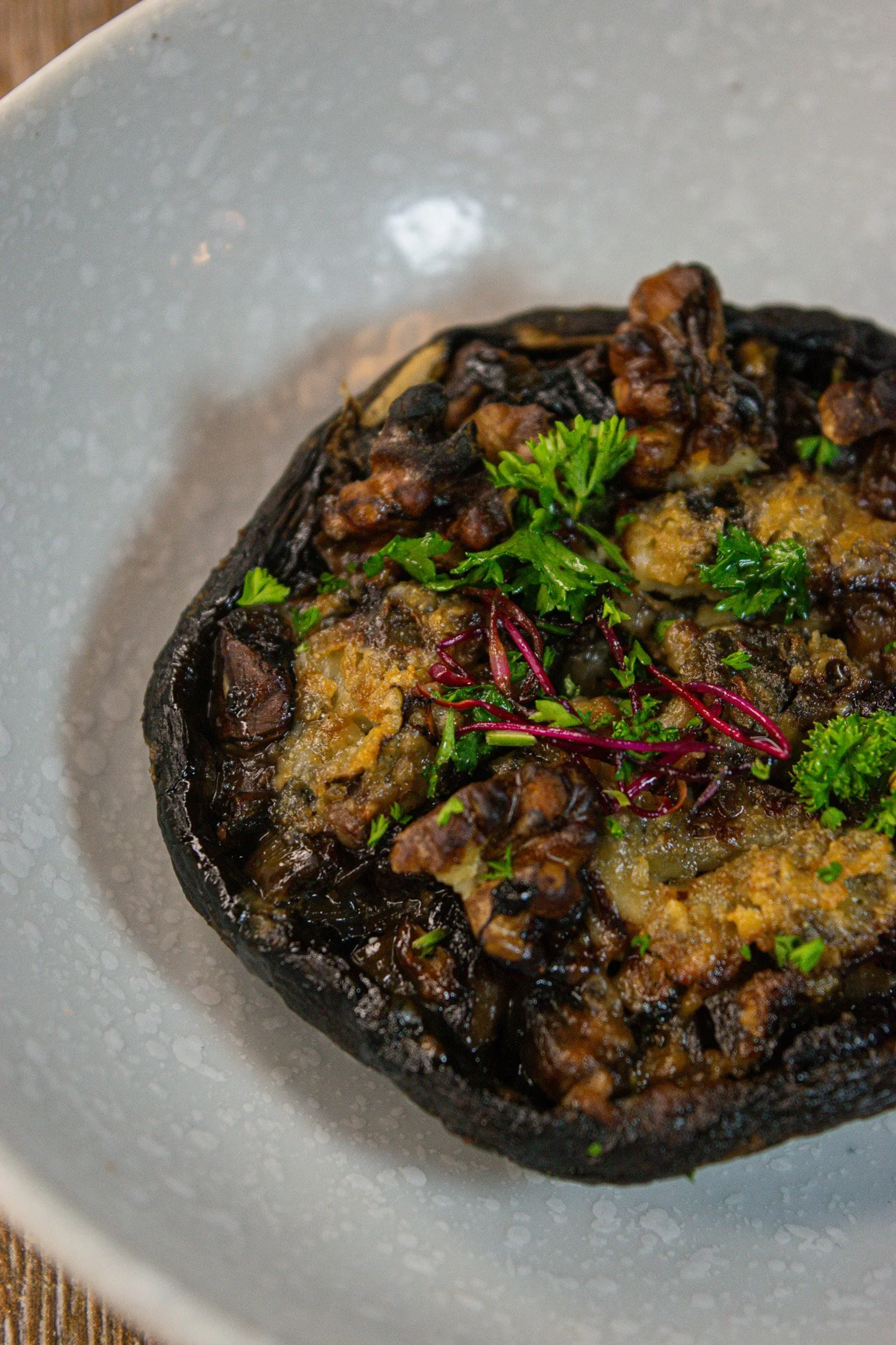 Close-up of a stuffed mushroom topped with herbs on a white plate.