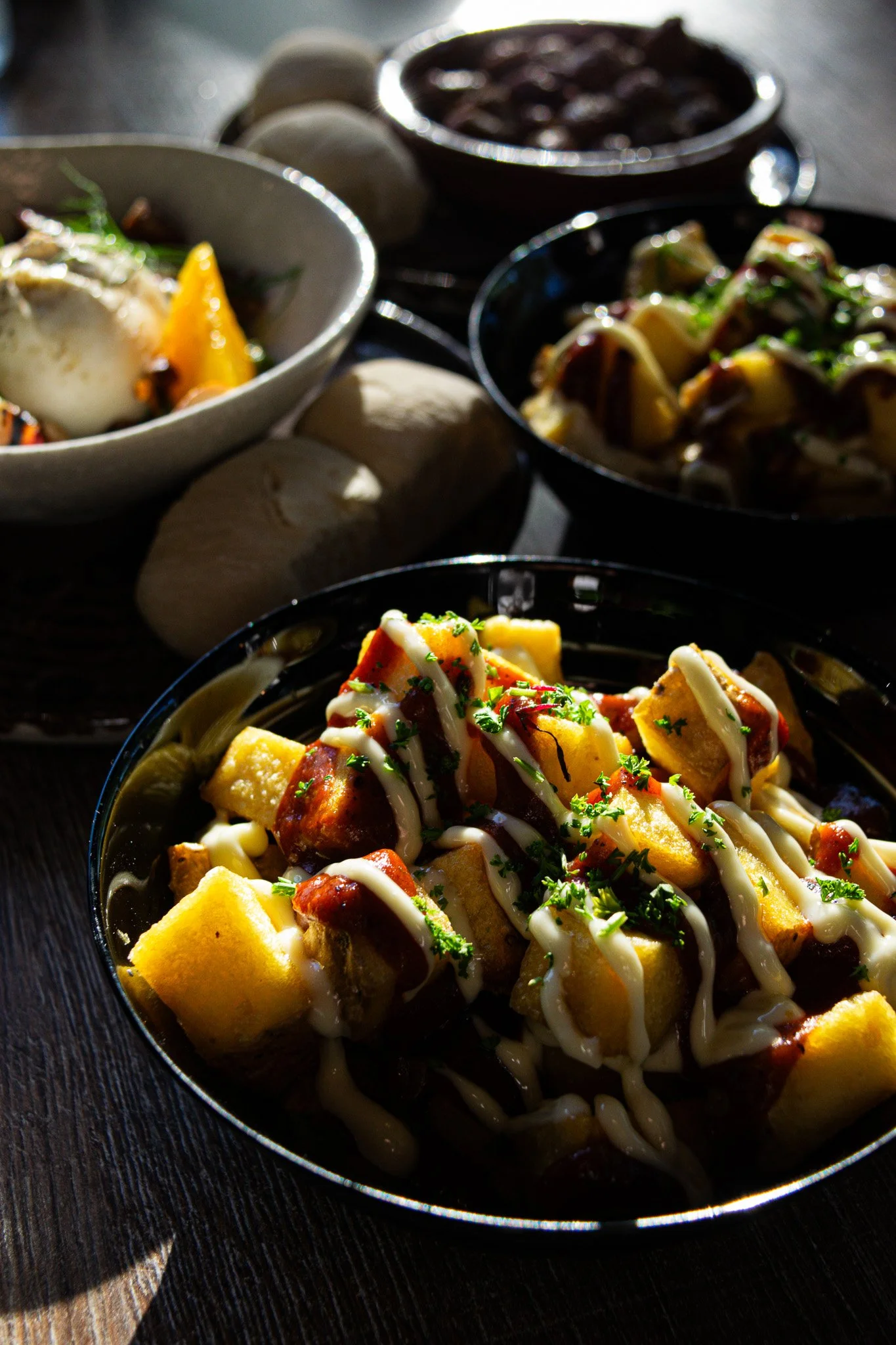 Close-up of a bowl of Asian noodle salad topped with chopped herbs and drizzled with white dressing, with other bowls of food in the background on a dark wooden surface.