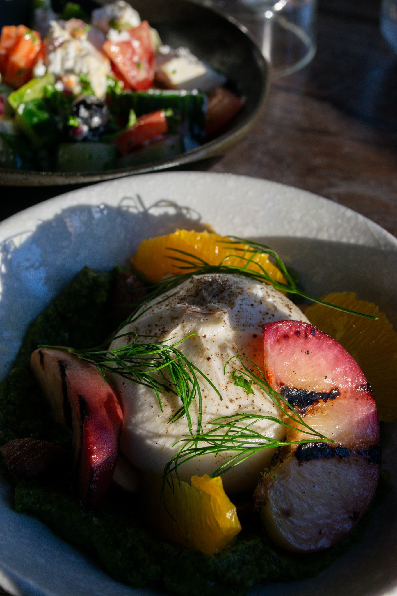 Poached egg topped with herbs, served with slices of meat (possibly ham or bacon), surrounded by yellow bell peppers, with a side of roasted vegetables in a bowl in the background.