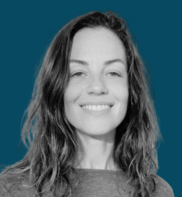 Retrato de uma mulher com cabelo castanho ondulado, sorrindo, contra um fundo azul.