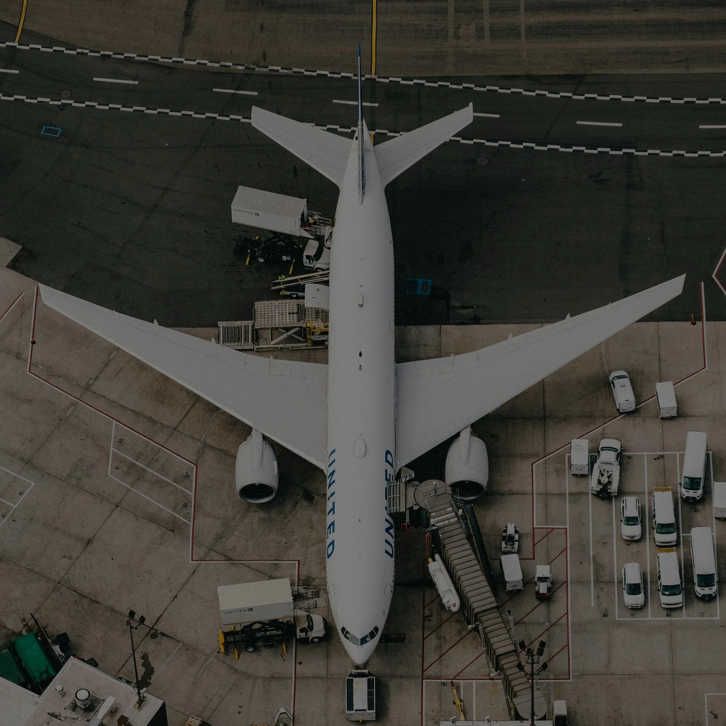 An overhead view of a United Airlines aircraft parked at an airport gate, surrounded by ground service vehicles and equipment.