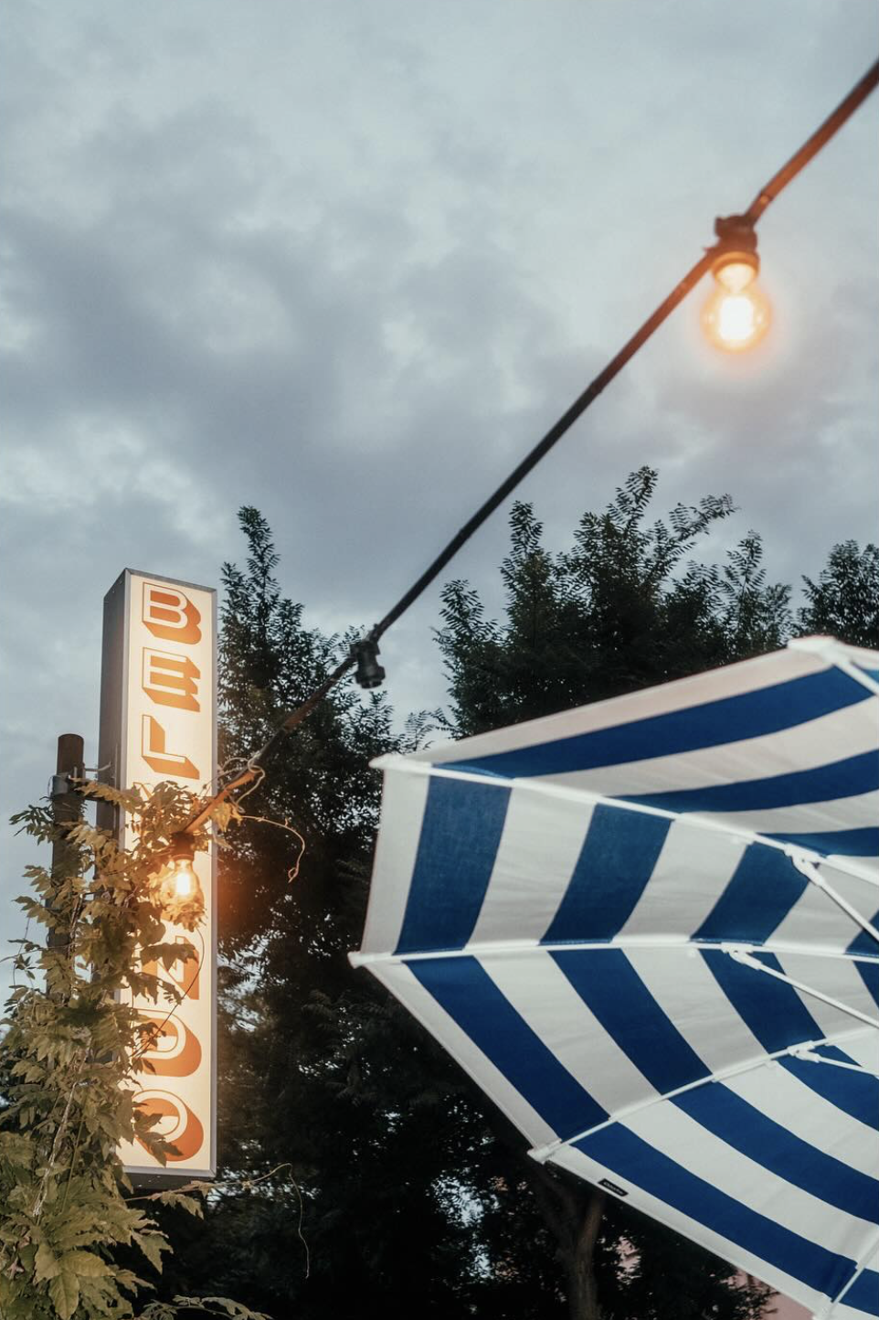 Alla Mano pop-up location with Belmondo sign, striped terrace umbrella and warm evening lights in Zurich.