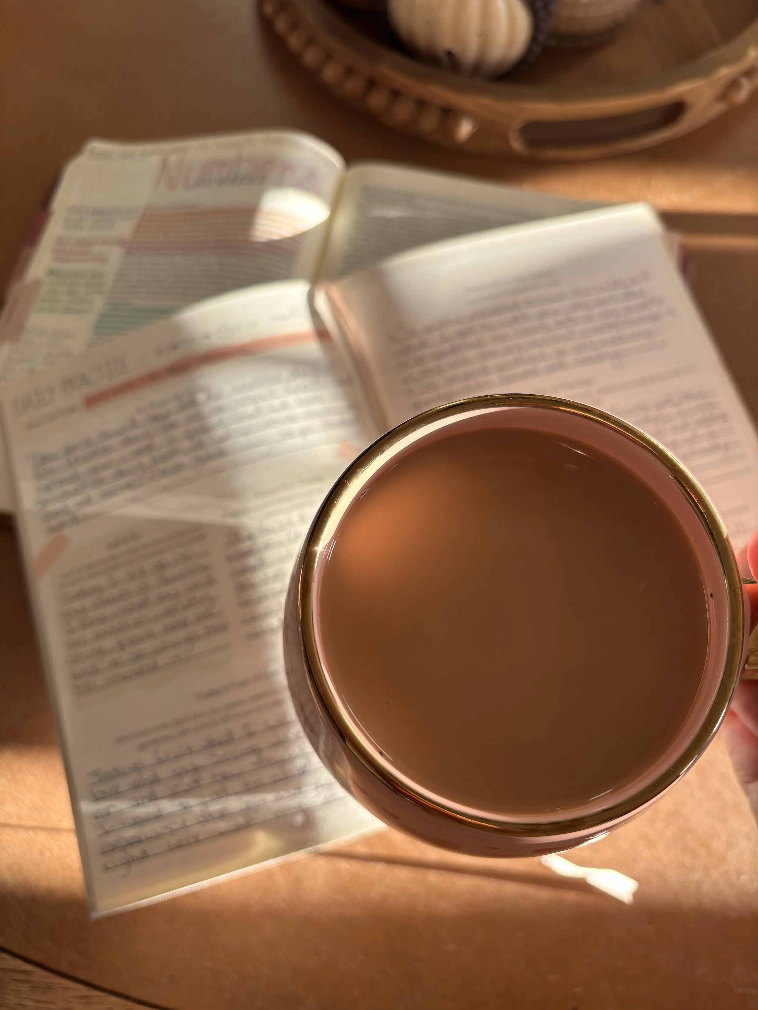 A cup of hot chocolate on a wooden table next to a faith based journal and her bible