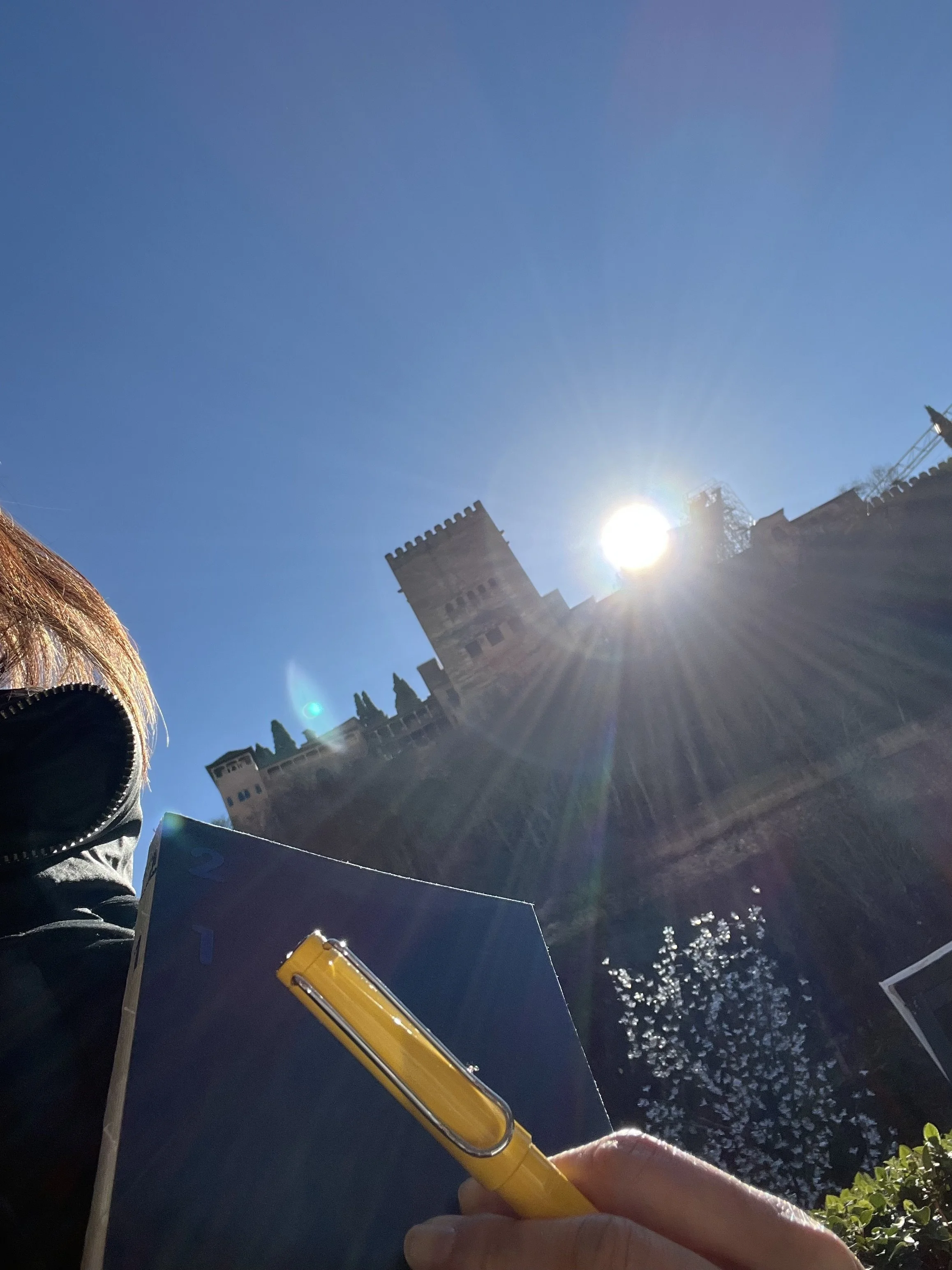 Close-up of a person's hand holding a yellow highlighter pen, with a sunset over a castle and clear blue sky in the background