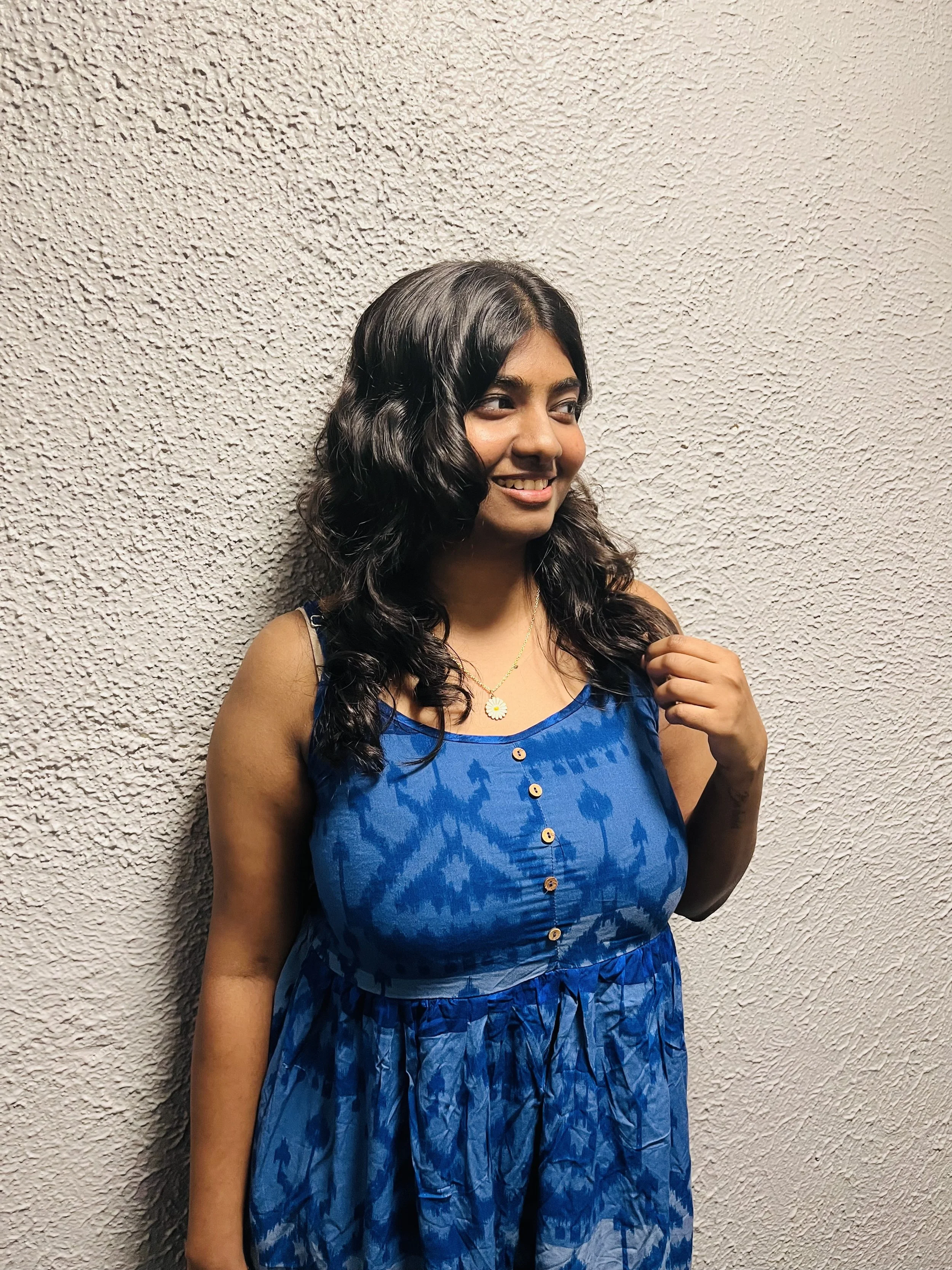 Smiling woman in a blue dress with a textured wall background.