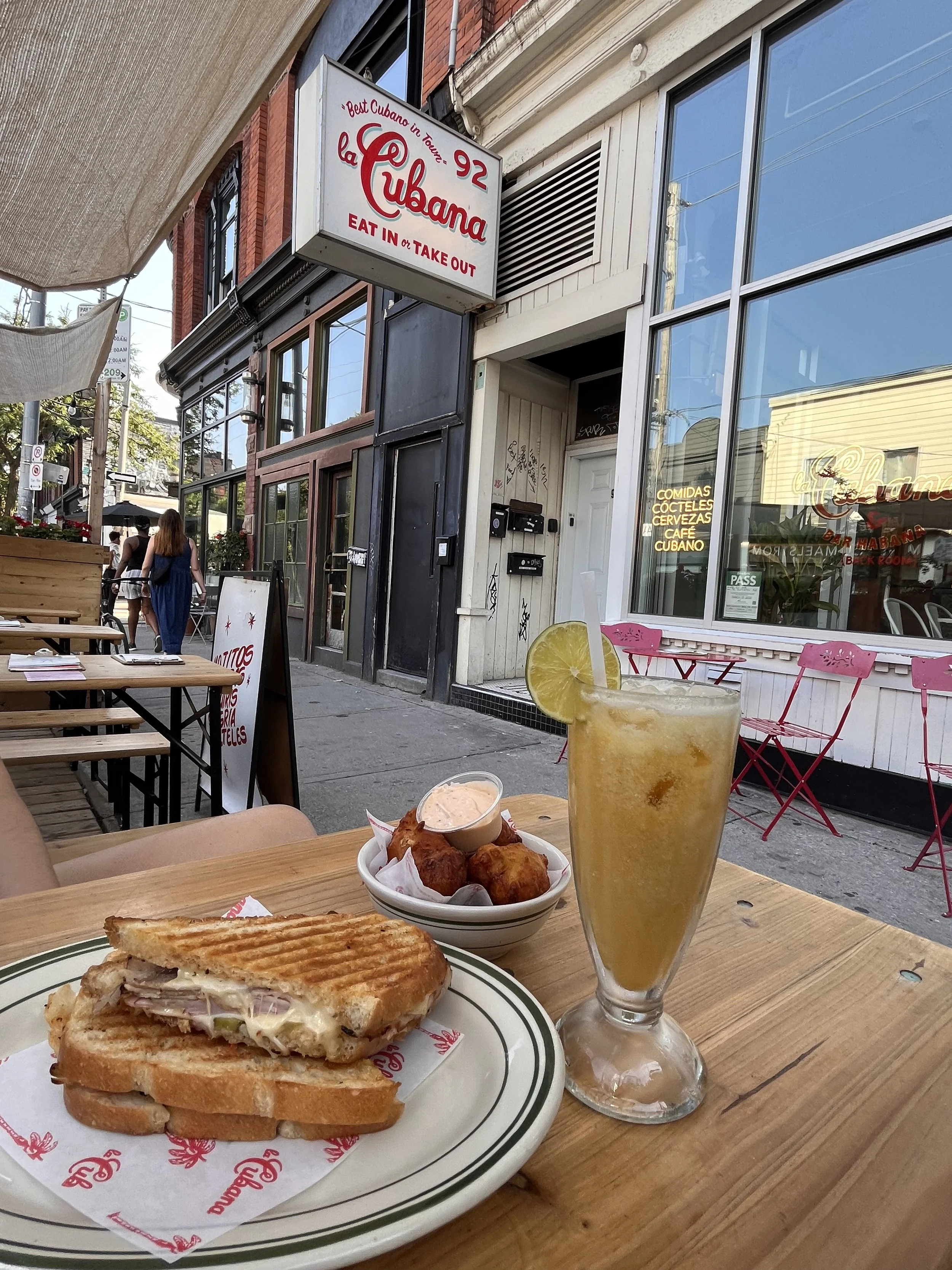 Cuban sandwich and drink at outdoor table in front of "La Cubana" restaurant.