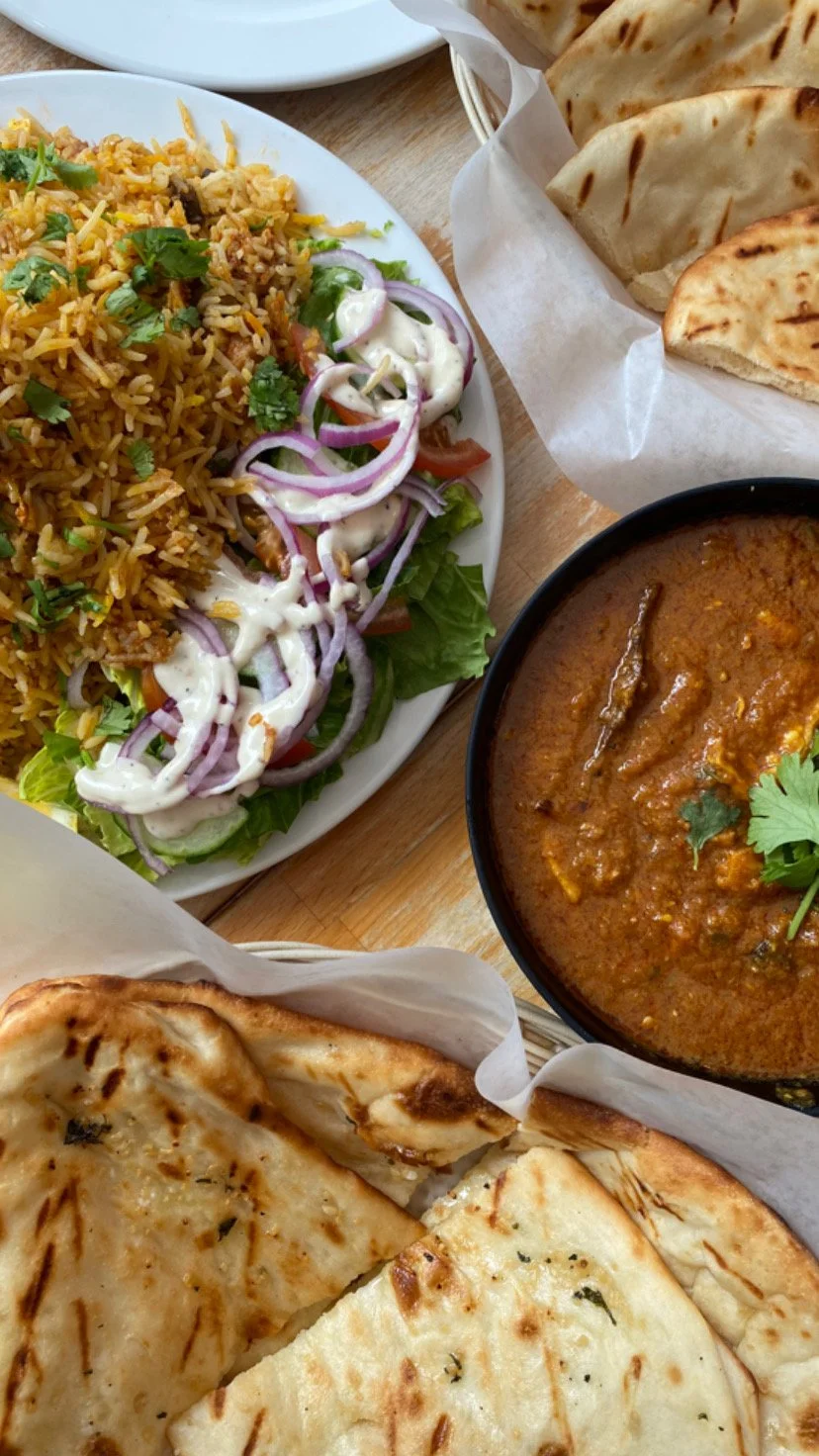 Indian meal with biryani, curry, salad, and naan bread on a table.
