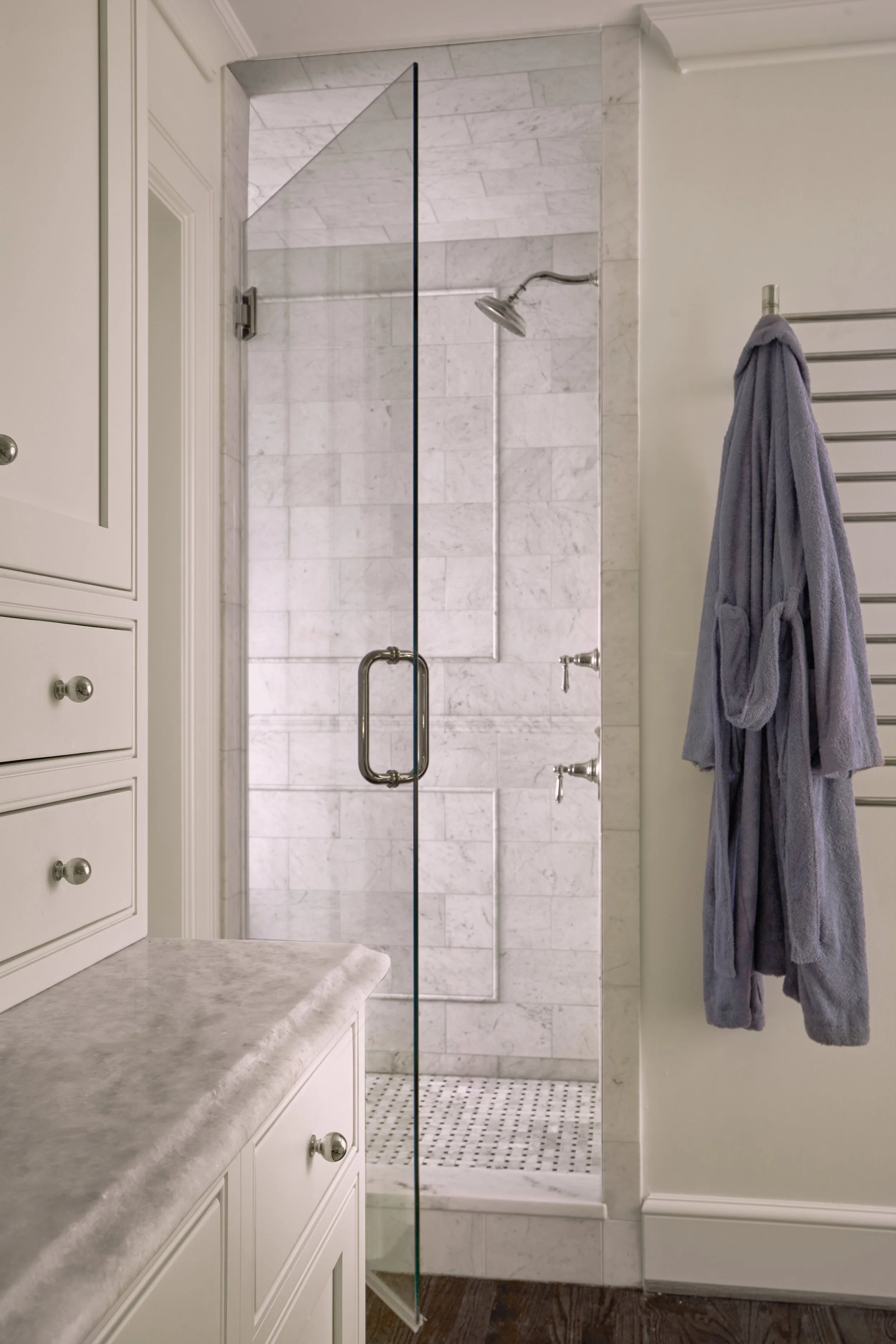 Bathroom with a glass door shower, marble walls, and a towel hanging on a towel rack.