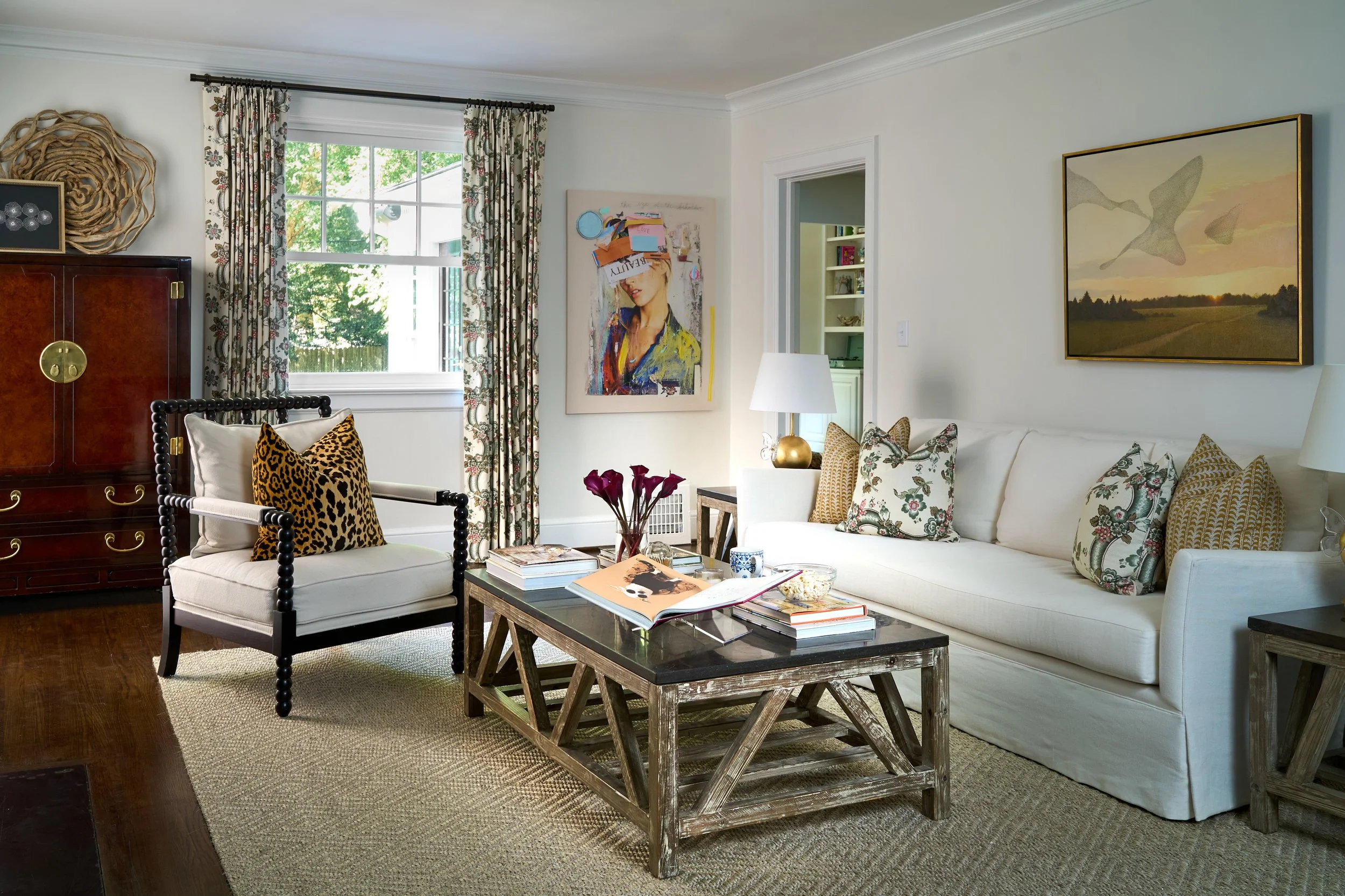 A cozy and collected living room featuring original art work, a beautiful vintage mahogany bar cabinet and inviting seating.