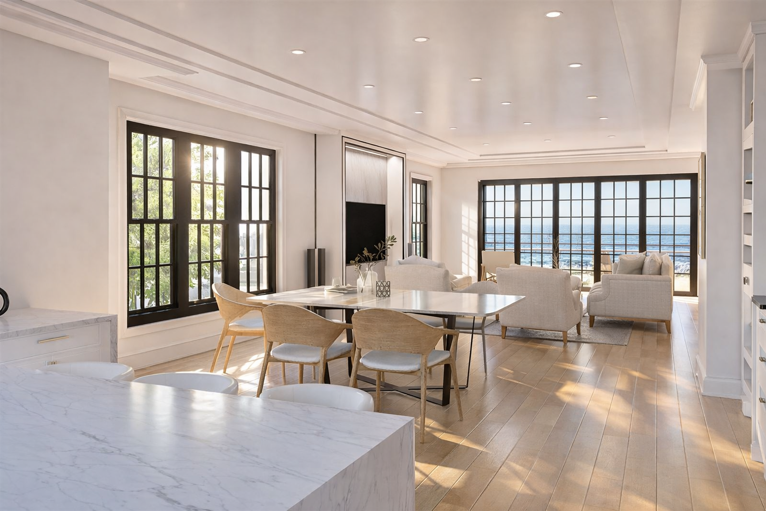 Bright living room and dining area with large windows showing a view of water, furnished with white sofas, wooden chairs, and a marble table.