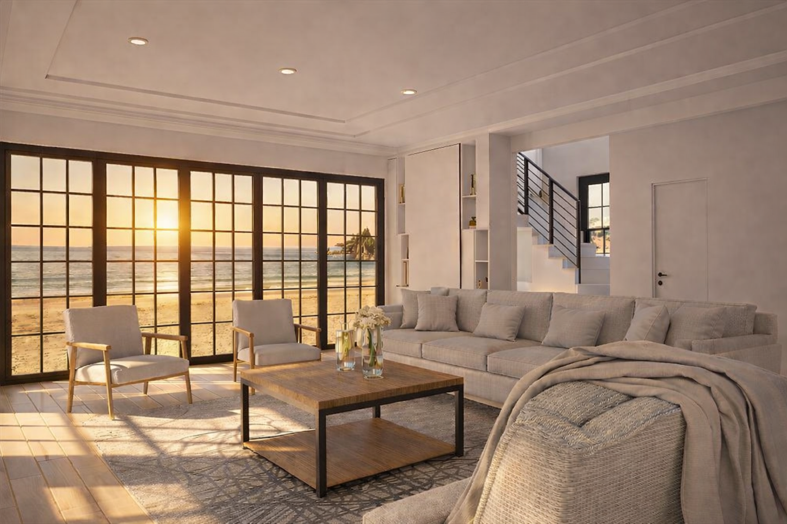 Living room with large windows overlooking a beach at sunset, white sofa, armchairs, coffee table with vases of flowers, neutral color scheme, staircase in the background.