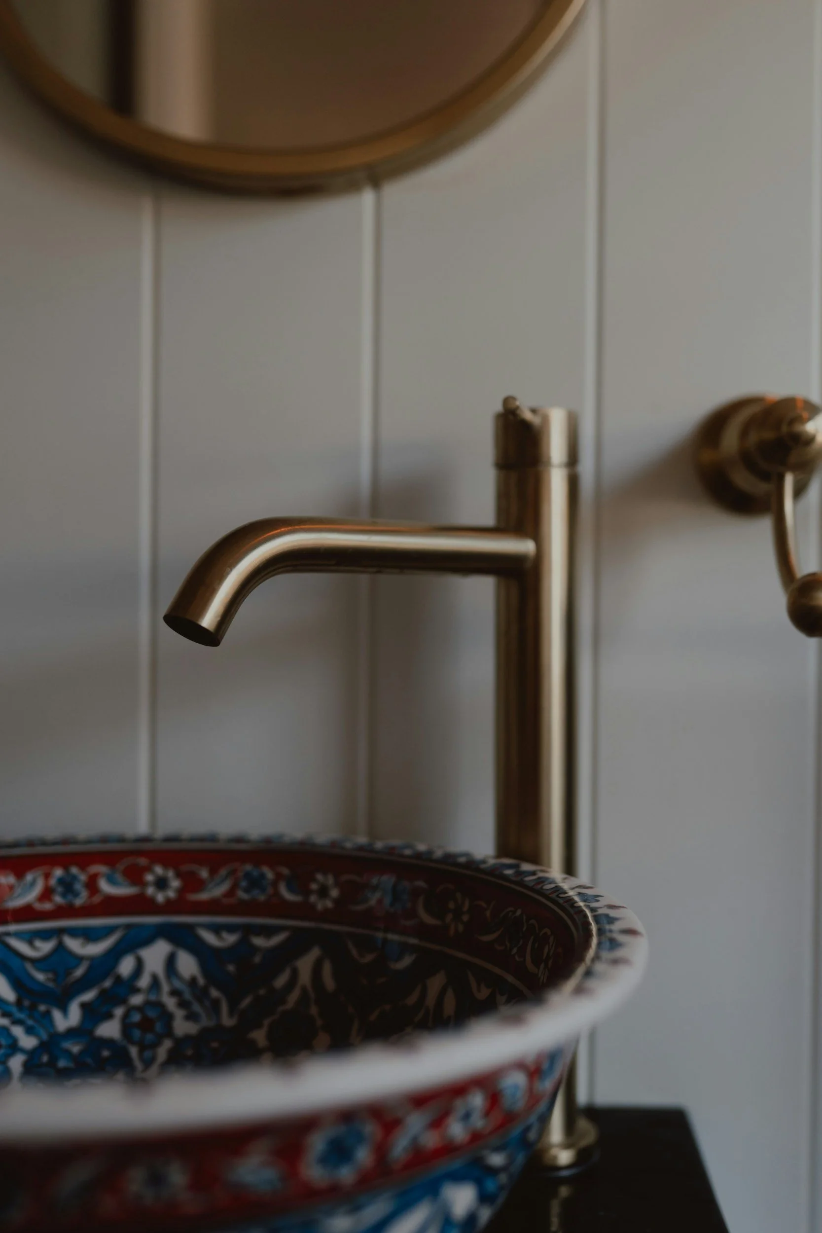Close-up of a gold-colored faucet above a decorative ceramic bowl with intricate floral and geometric pattern.