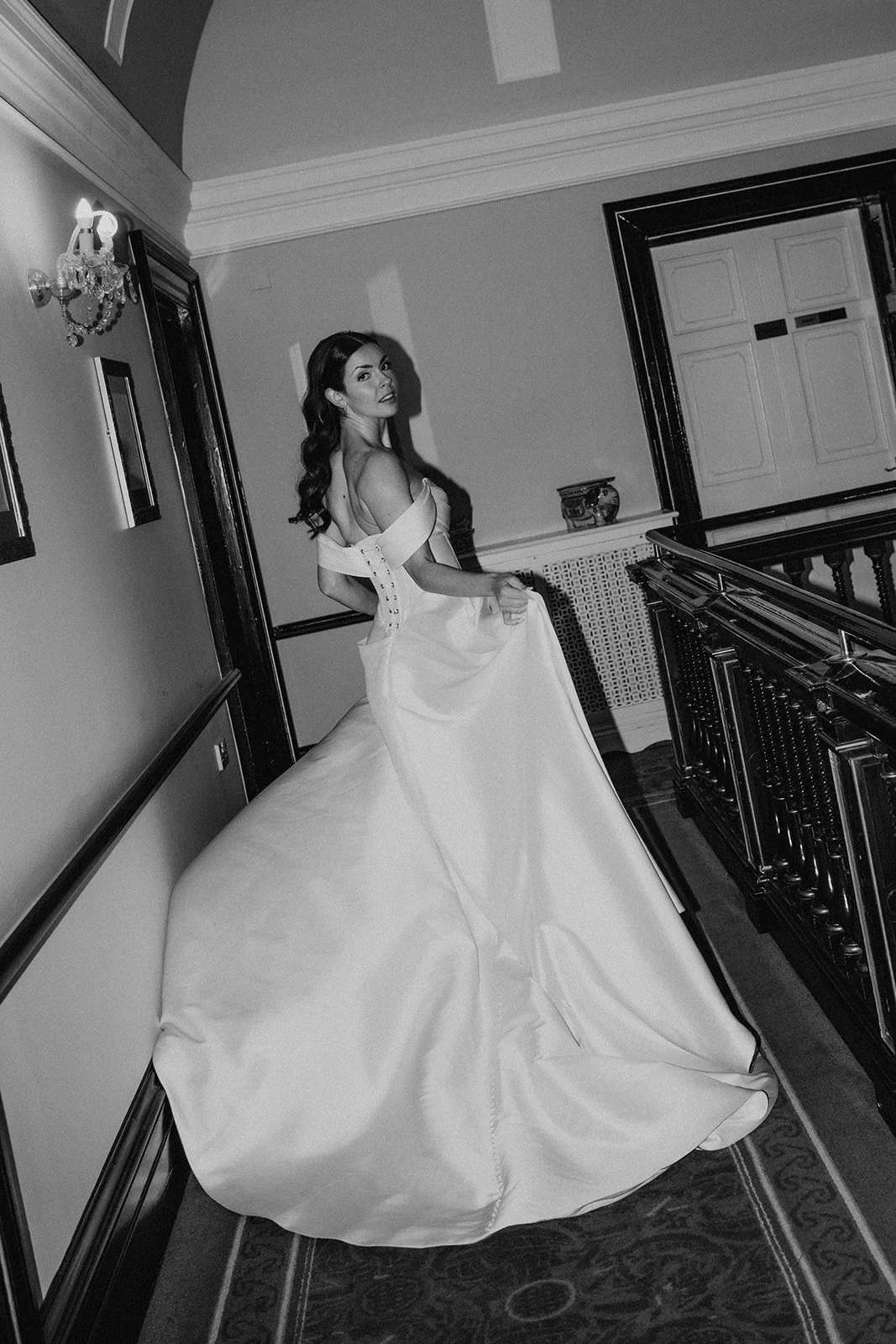 A woman in a wedding gown sitting on a curved bench in an elegant, vintage-style room with a chandelier and ornate details.