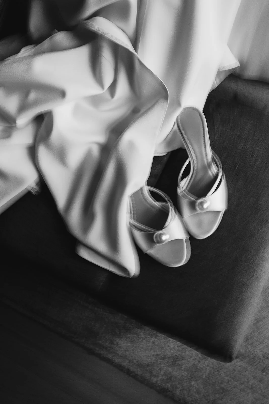Pair of satin shoes with high heels placed on a dark fabric surface, with a satin garment draped next to them.