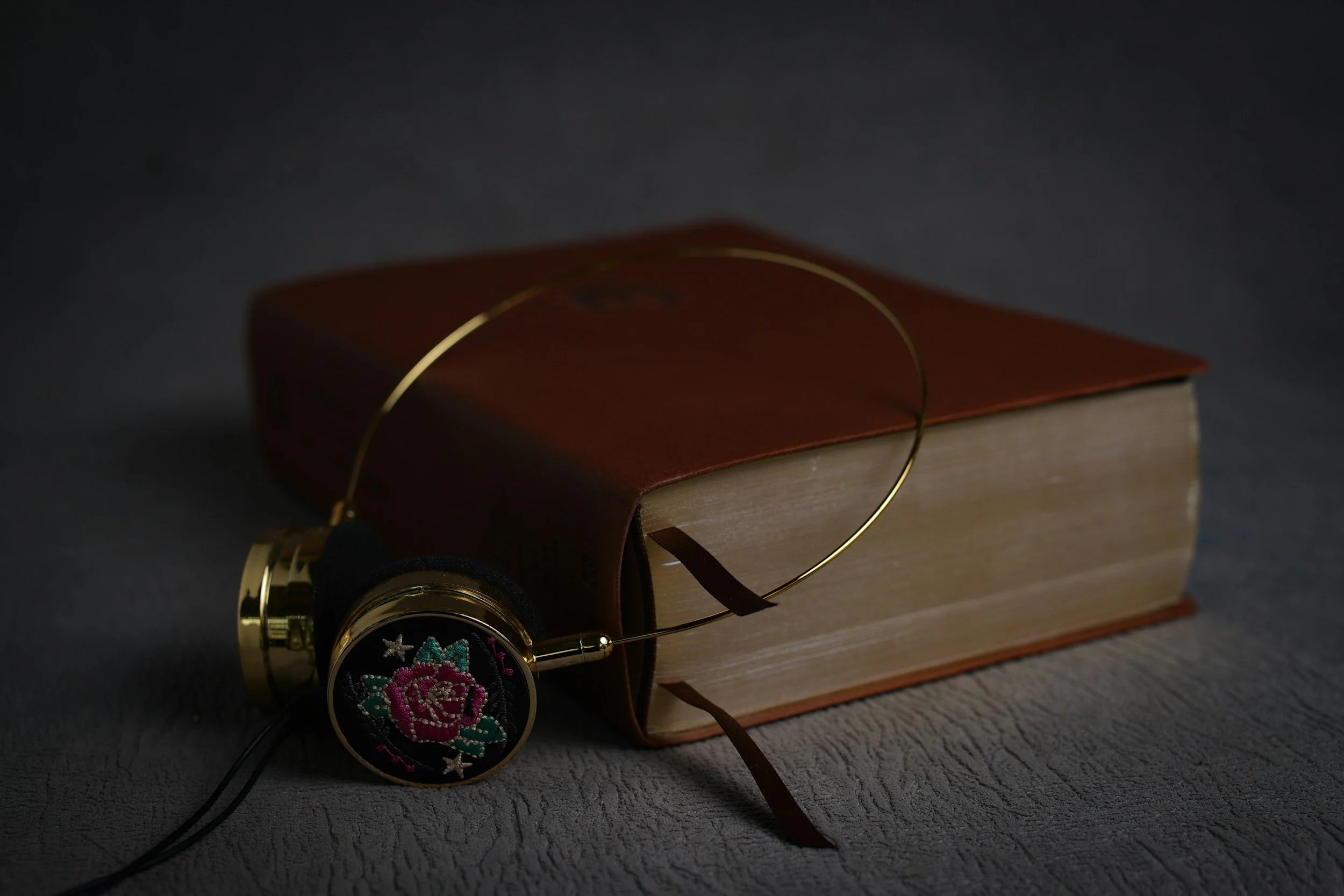 A vintage camera with floral embroidery on the lens cap, placed on a wooden book with a brown cover, against a dark background.