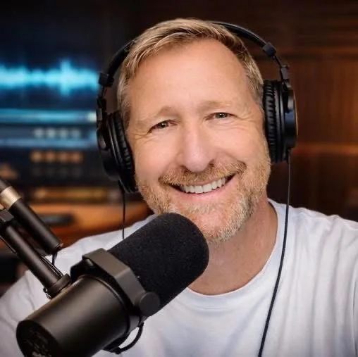 Man with headphones smiling into a microphone in a recording studio.