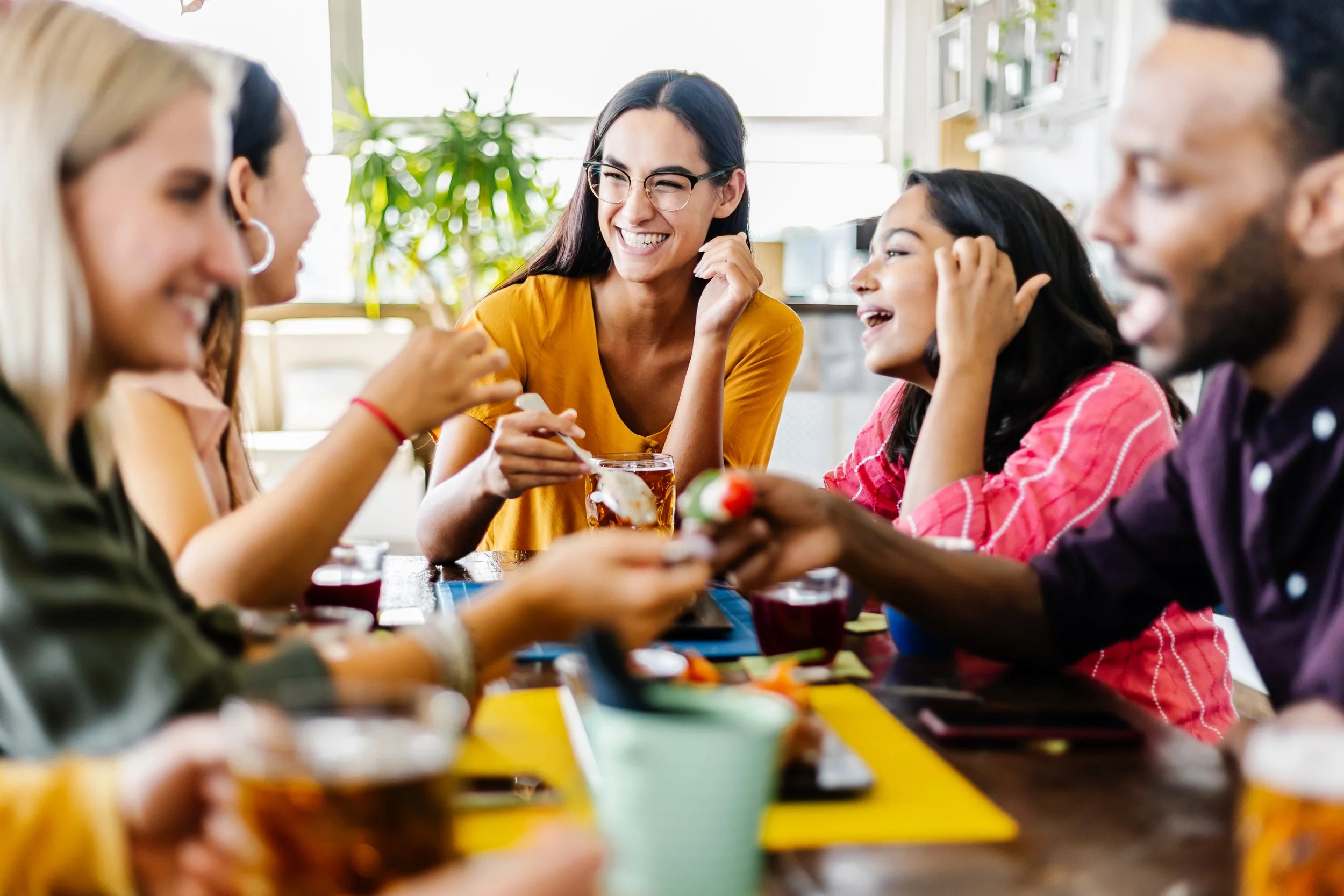 Group of diverse young adults enjoying drinks and conversation at a social gathering in a bright, modern cafe or restaurant.