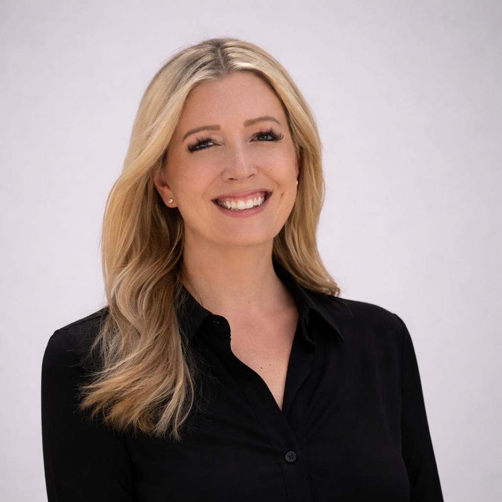 A smiling blonde woman with wavy hair wearing a black button-up shirt against a plain light gray background.