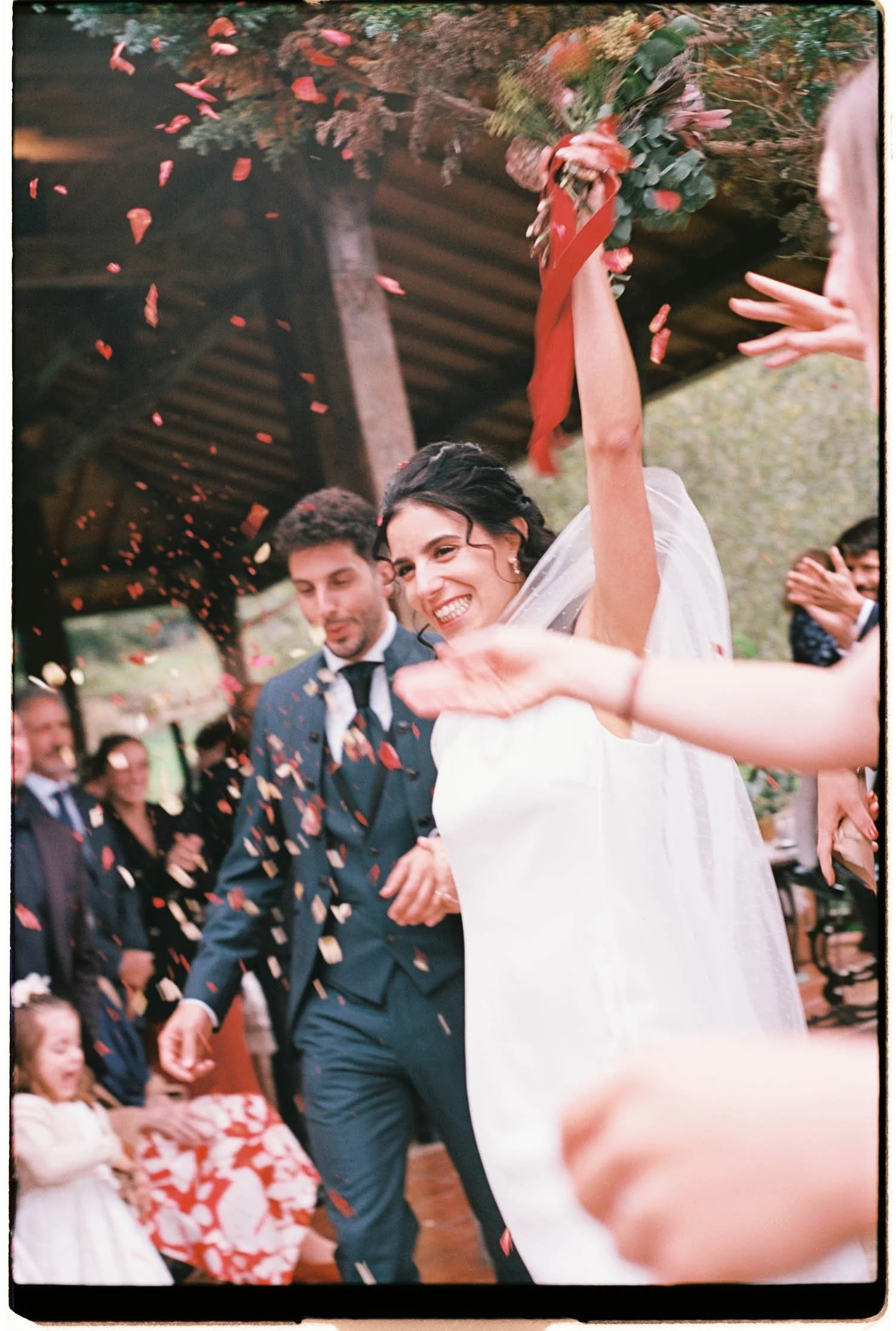 Couple just married walking happily, celebrating. Flower petals are falling in the air.