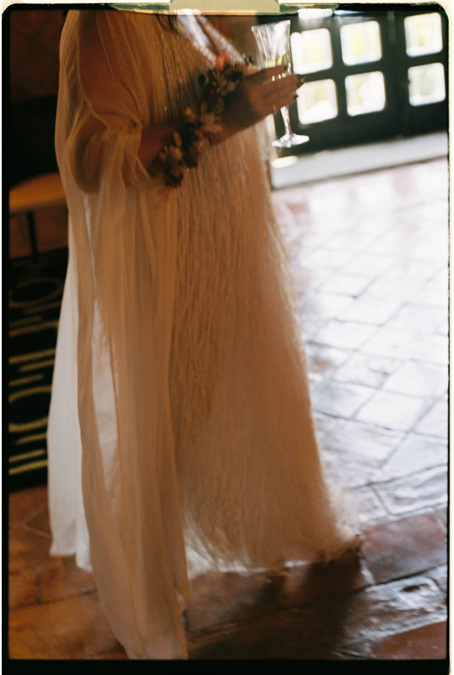 Person wearing a dress taking a photo with a phone in a room with wooden flooring and a large window in the background.