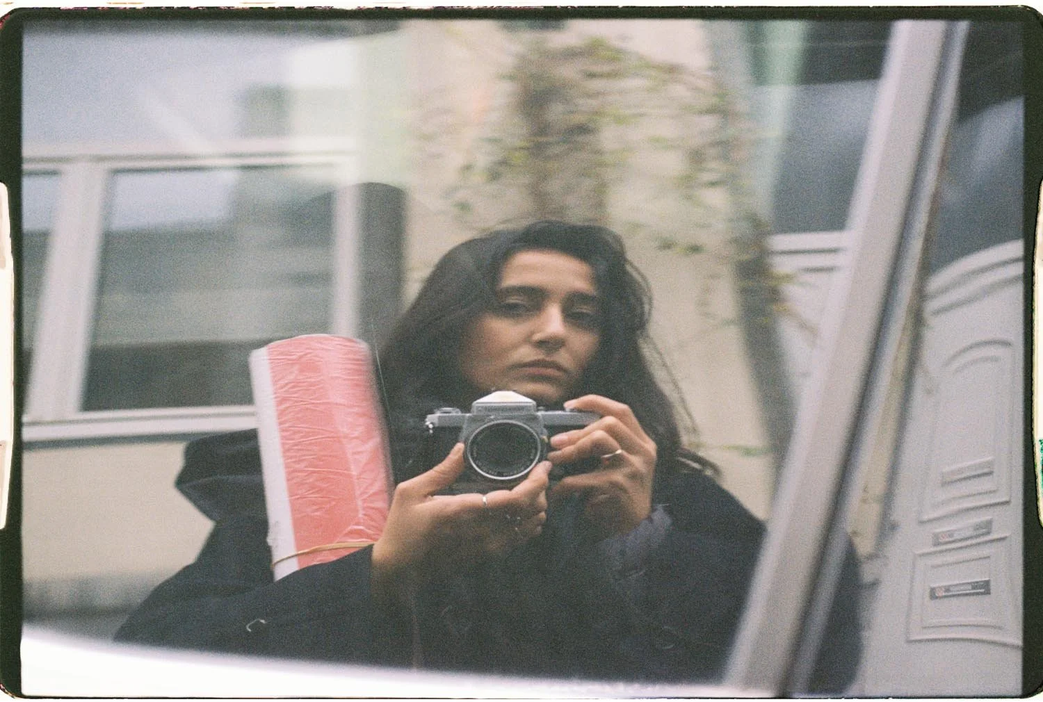 A woman taking a selfie with a camera in a mirror, carrying a rolled-up pink poster.