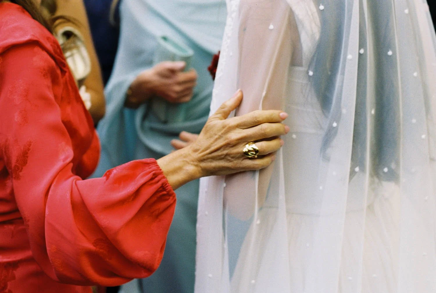 Analogue close-up of a bride's mother wearing a red satin blouse, touching the bride's arm gently.