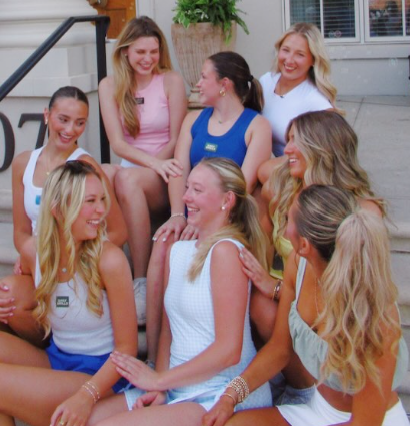 Group of eight young women sitting and laughing together outdoors on a sunny day.