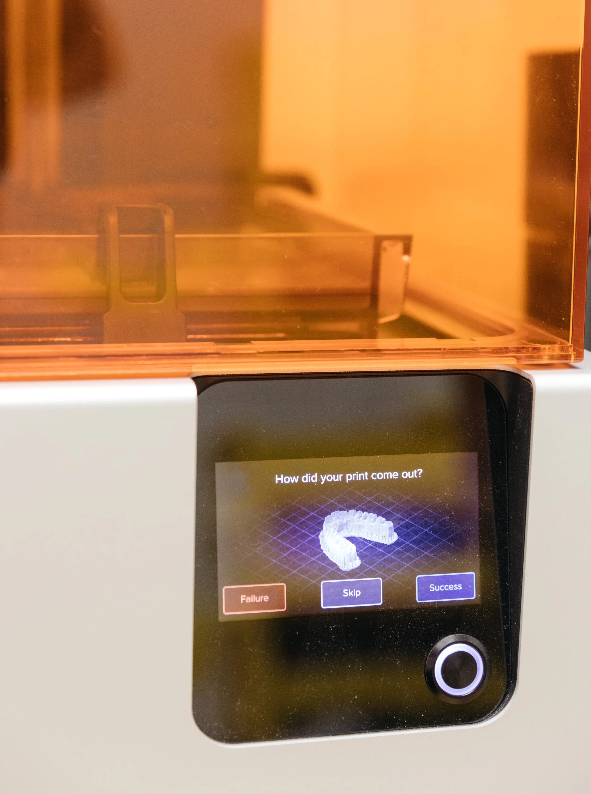 A 3D printer with a screen showing a digital model of a snake and options for success, failure, or skipping, in front of a warm-colored enclosure.