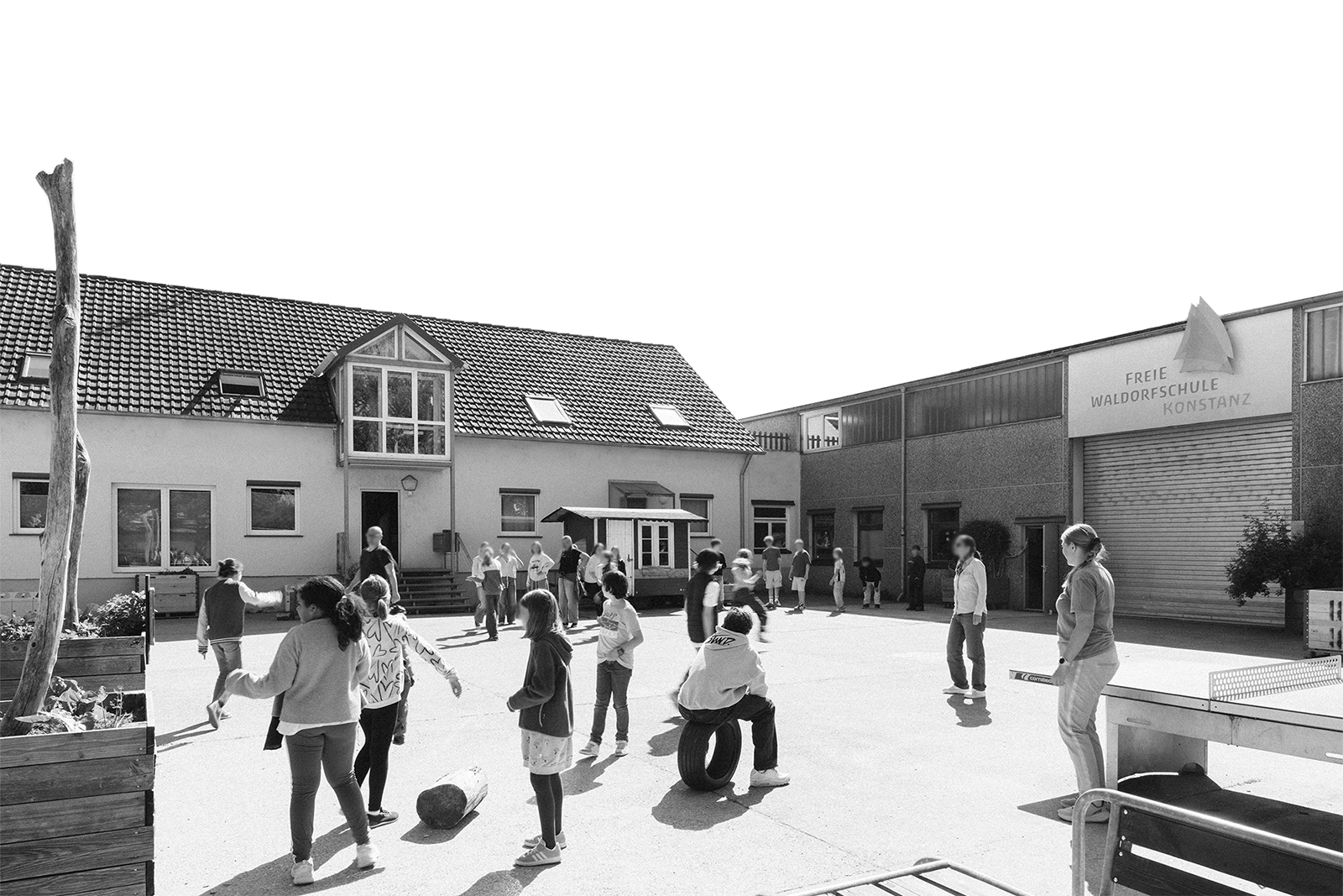 Kinder spielen auf dem Schulhof einer Waldorfschule in Konstanz, einige stehen, andere spielen mit Reifen und Steinen, Gebäude im Hintergrund, schwarz-weiß Aufnahme.