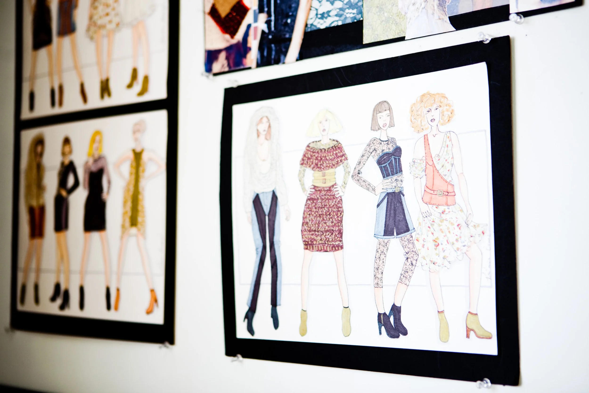 Illustrations of women modeling various outfits are displayed on a wall. The drawings depict different fashion styles, featuring diverse clothing and footwear.