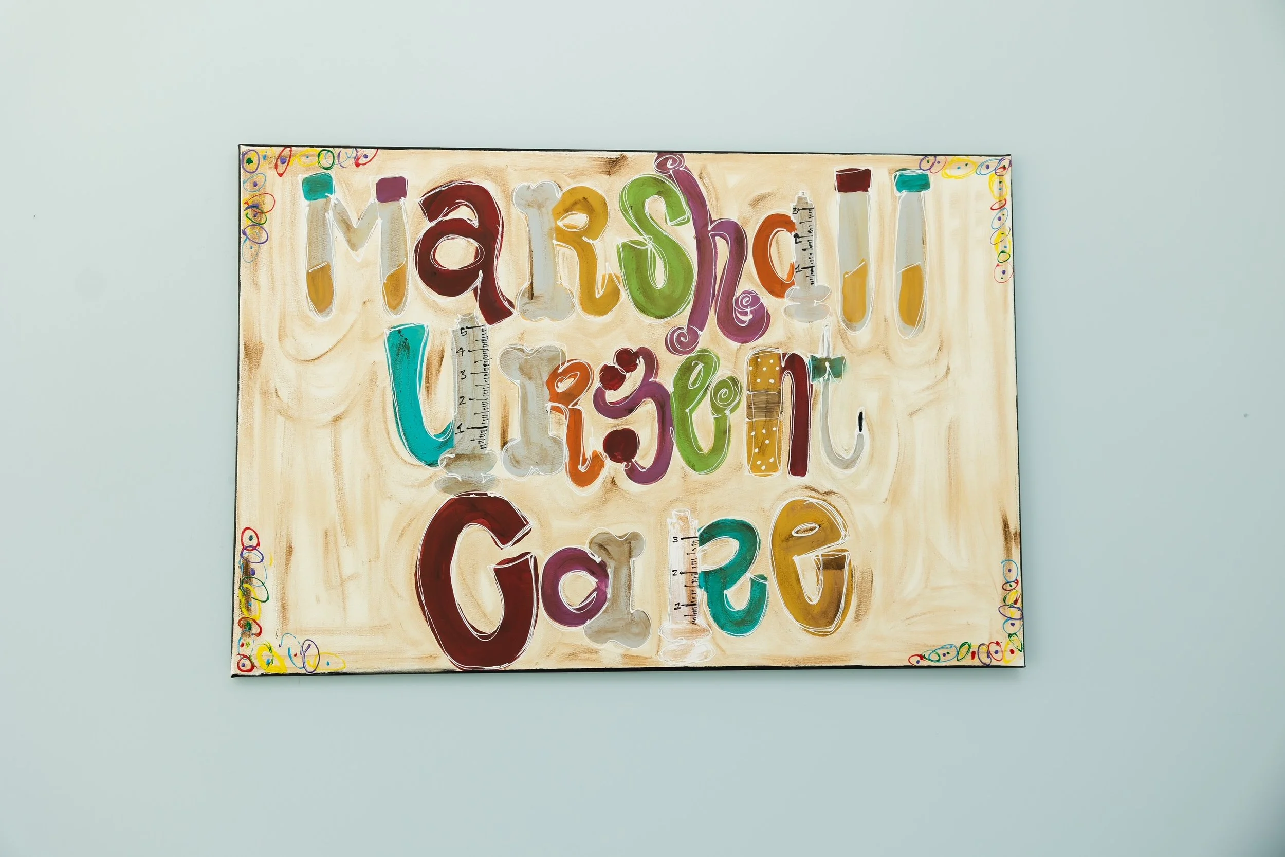 Colorful painted artwork spelling 'march' with various letter styles and decorative elements on a beige background, framed with a border of multicolored circles and squiggles, mounted on a light-colored wall.