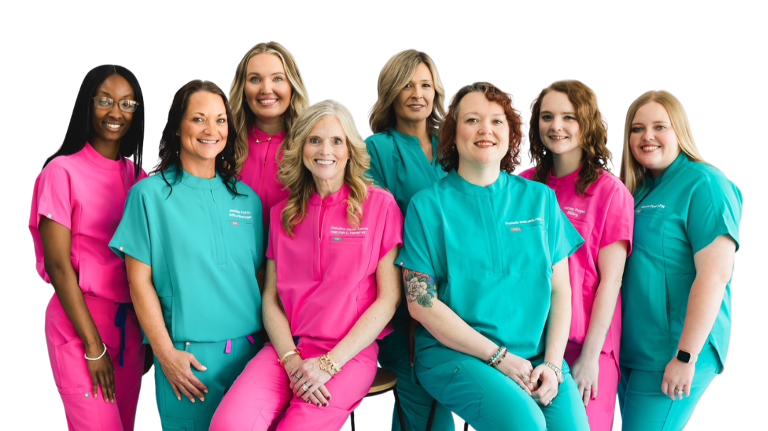 Group of nine healthcare professionals, eight women and one man, wearing scrubs in pink and teal, posing together against a white background.